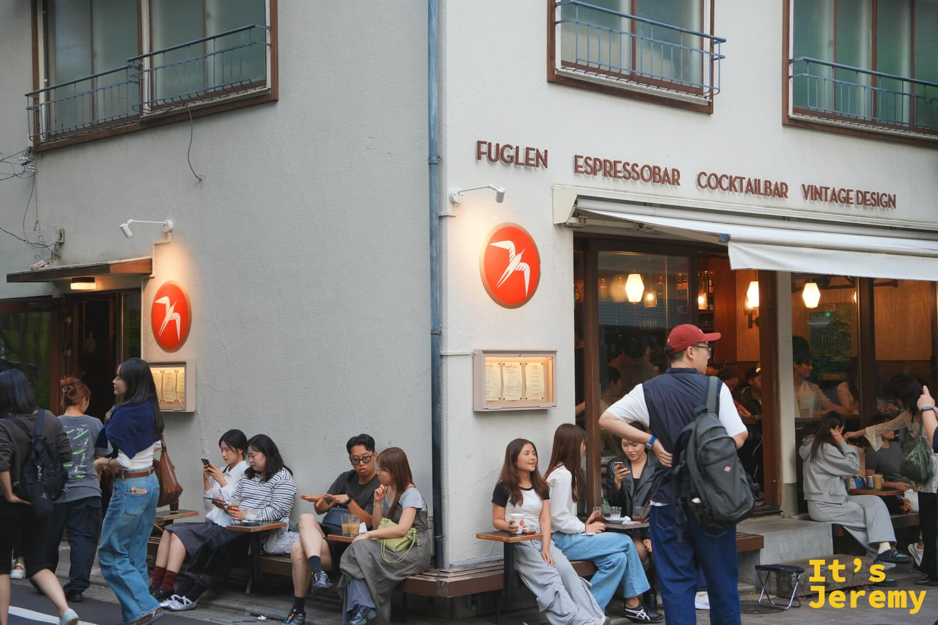 傍晚時分 Fuglen Tokyo 外觀,門口長椅坐滿人,整棟建築點燈後有一種溫暖的北歐感