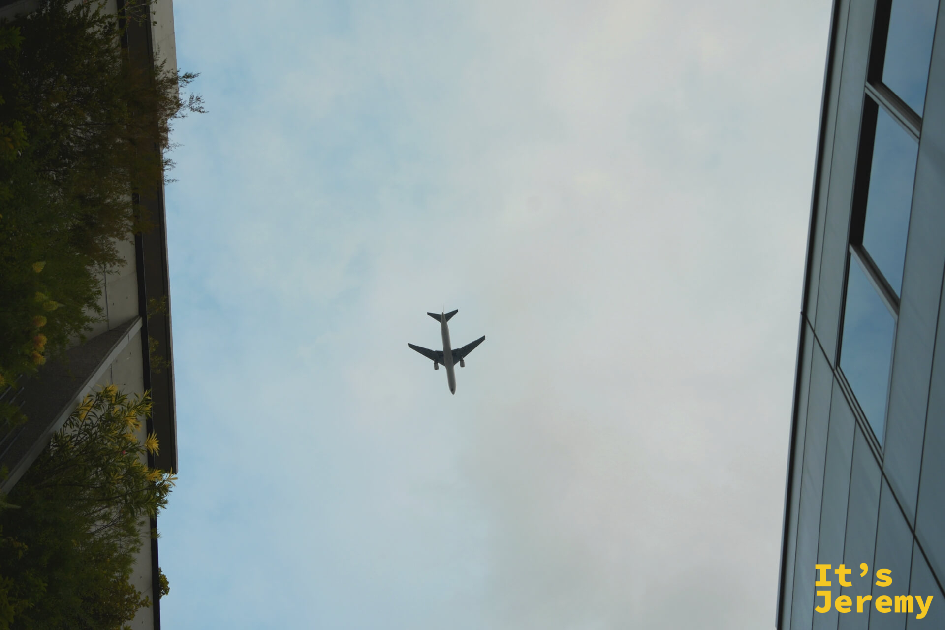 在表參道附近抬頭,一架飛機從兩棟建築之間的天空縫隙飛過,灰白天色,畫面乾淨
