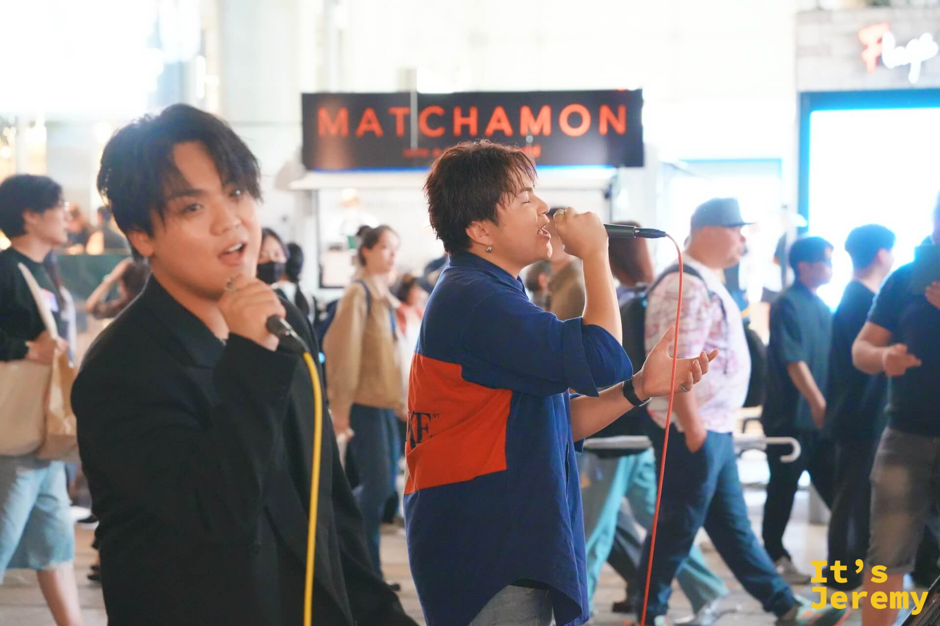 歌舞伎町セントラルロード旁的街頭表演,「MATCHAMON」橫幅高掛,兩位年輕男性拿麥克風熱情演唱,路人在旁圍觀