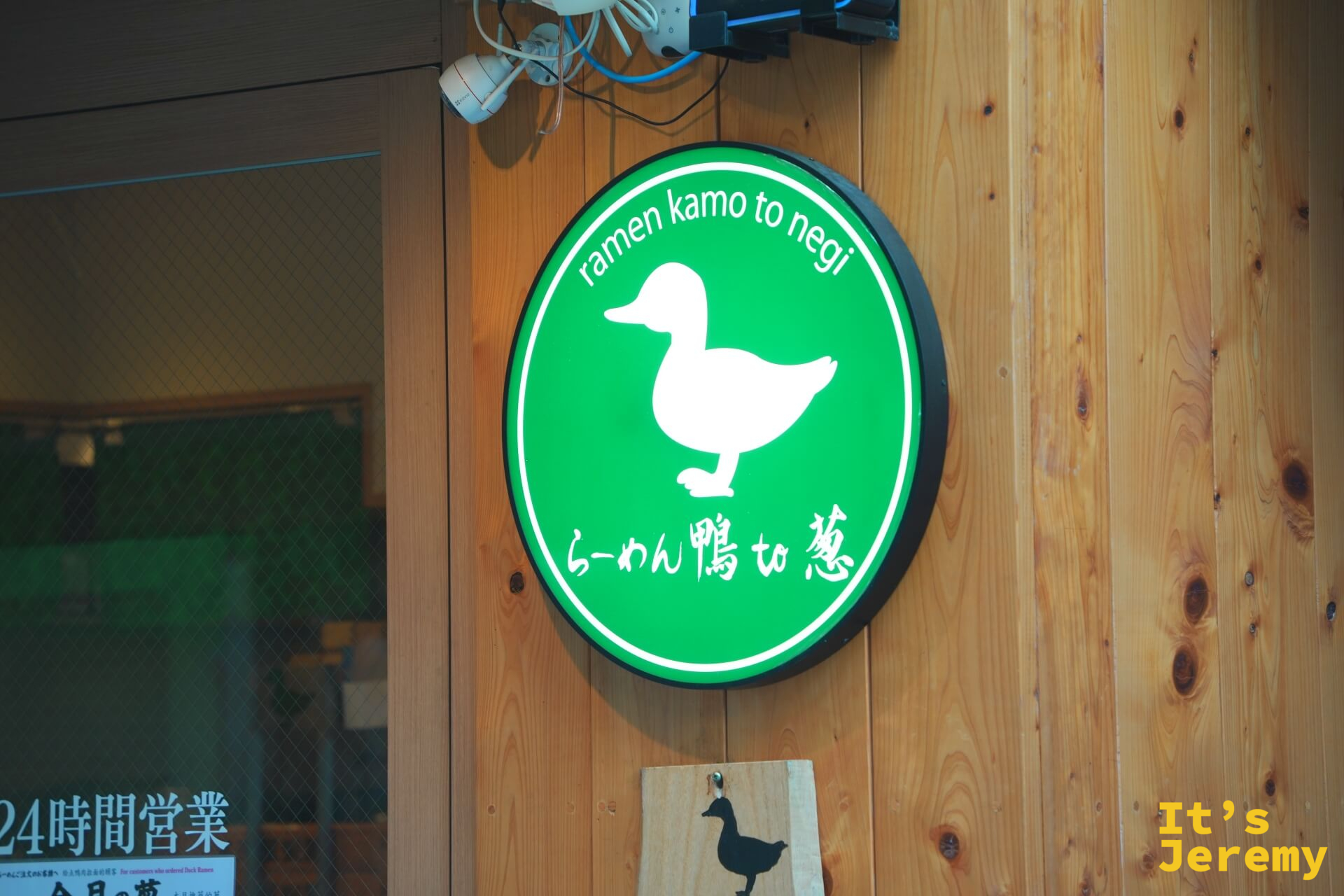 店門圓形logo燈箱,白色鴨子剪影在綠色底上,下方英文「ramen kamo to negi」