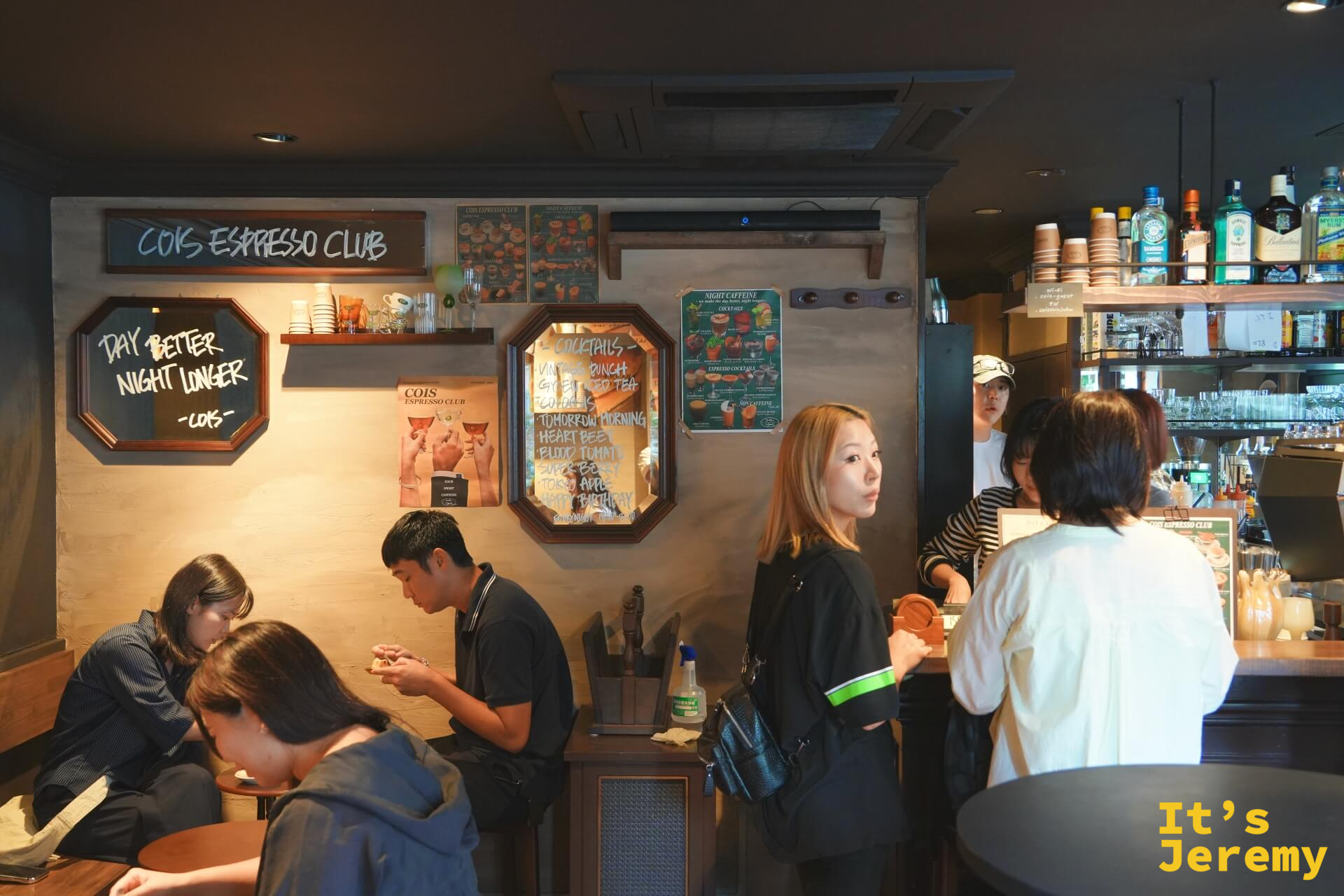 店內氛圍:客人在暖光下落座,「DAY BETTER NIGHT LONGER」手寫黑板與調酒菜單掛在同一面牆上
