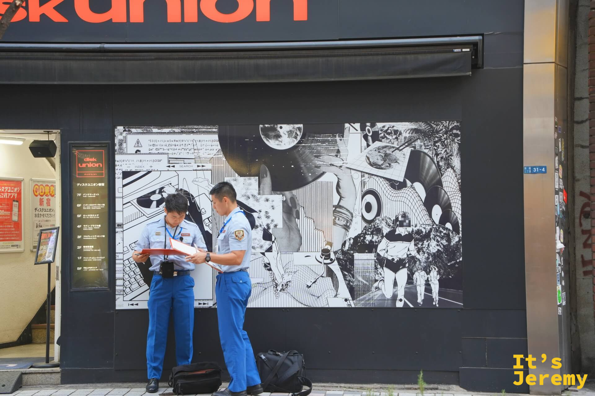 DiskUnion 新宿店外,兩名警察低頭核對文件,身後是店家外牆的大型黑白拼貼壁畫