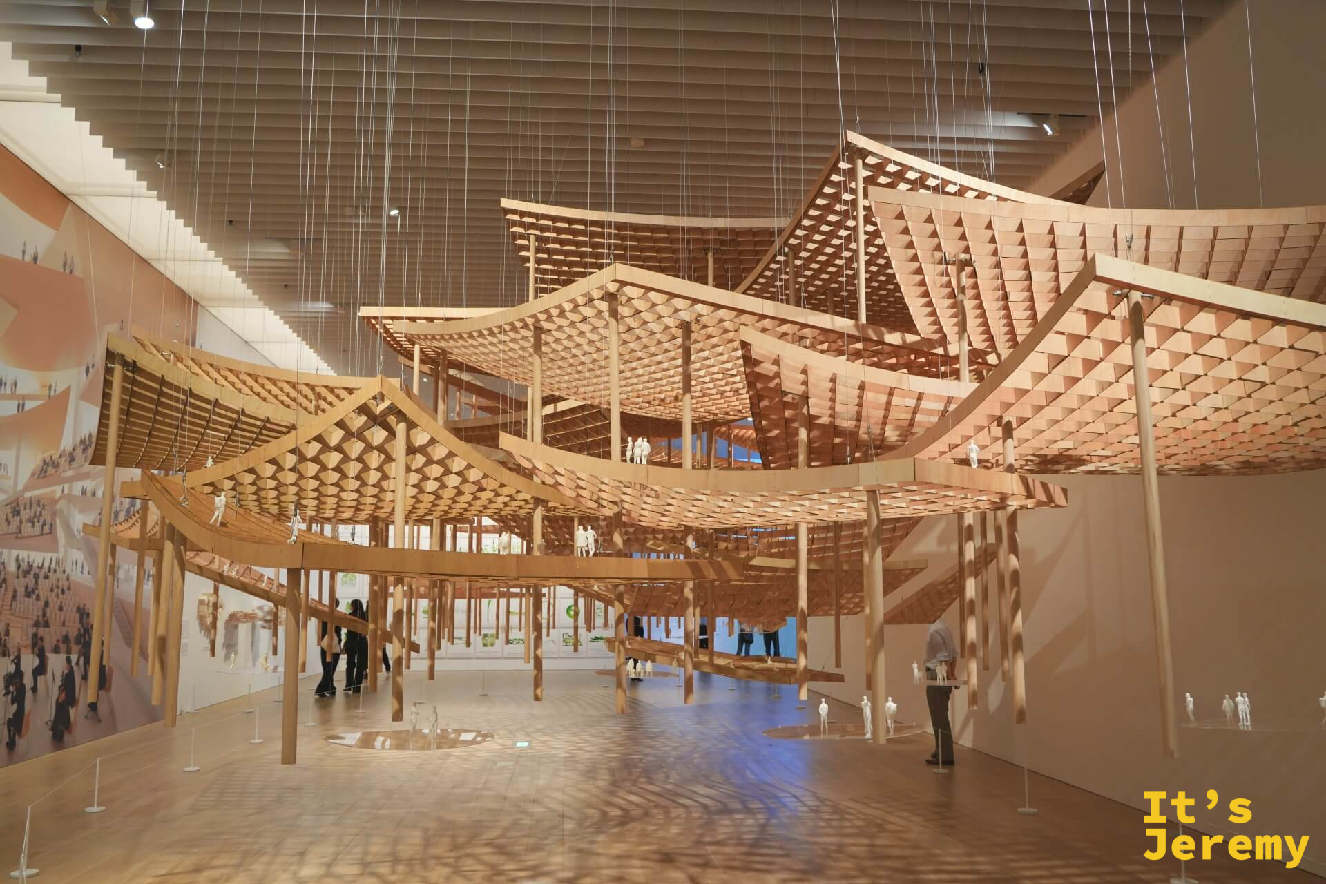 懸吊於展廳中央的波浪形大型木造建築模型，靠細鋼索從天花板垂落，白色人物模型點綴其間