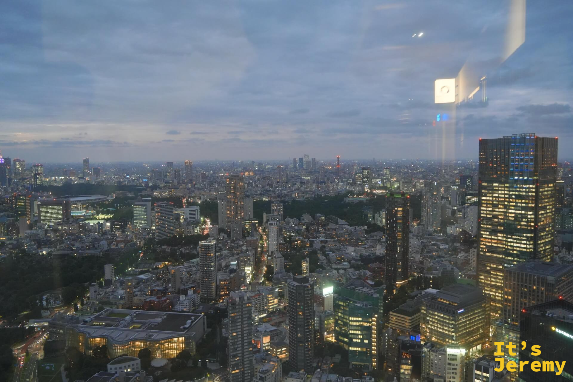 透過展廳玻璃窗望向東京黃昏全景，遠處可見東京鐵塔細長的輪廓