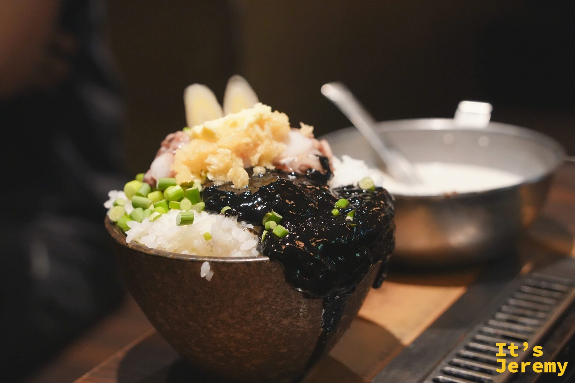 いか墨もんじゃ的食材在石碗裡,墨黑的醬汁裡有烏賊足和青蔥