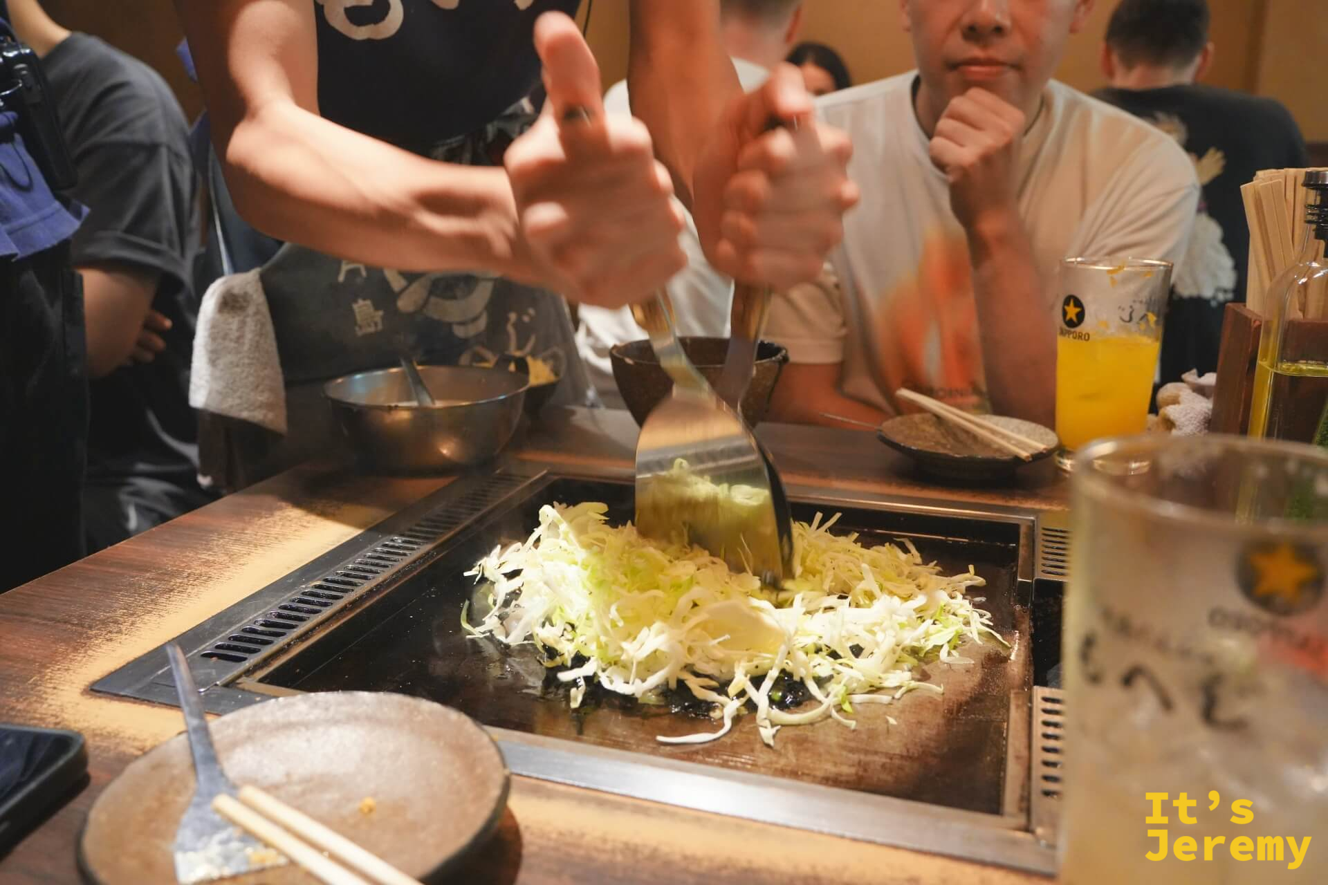 店員用兩把鐵鏟在鐵板上翻炒高麗菜絲,鋪平準備迎接文字燒麵糊
