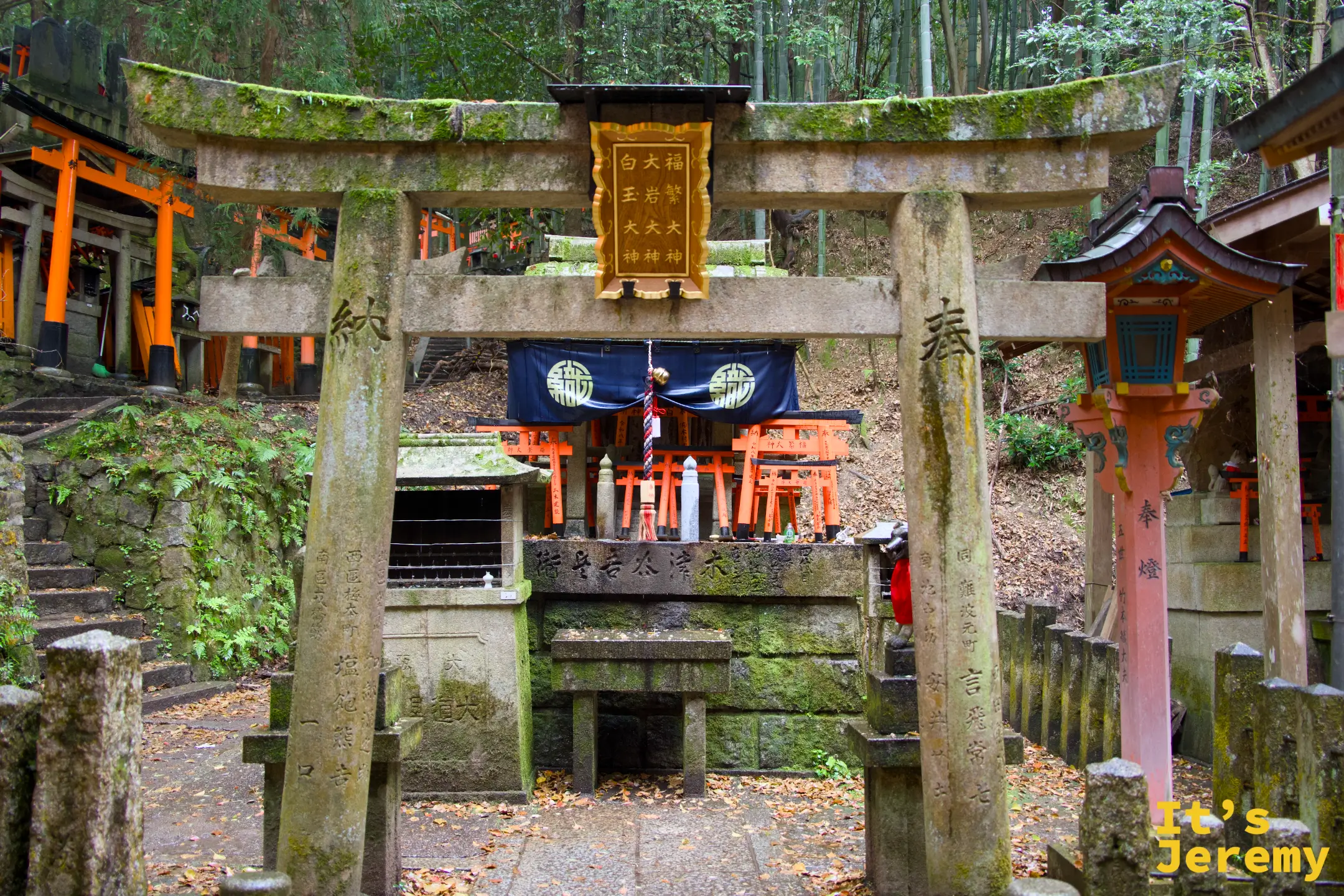 苔蘚包覆的石鳥居小祠，後方可見橙紅色的大鳥居