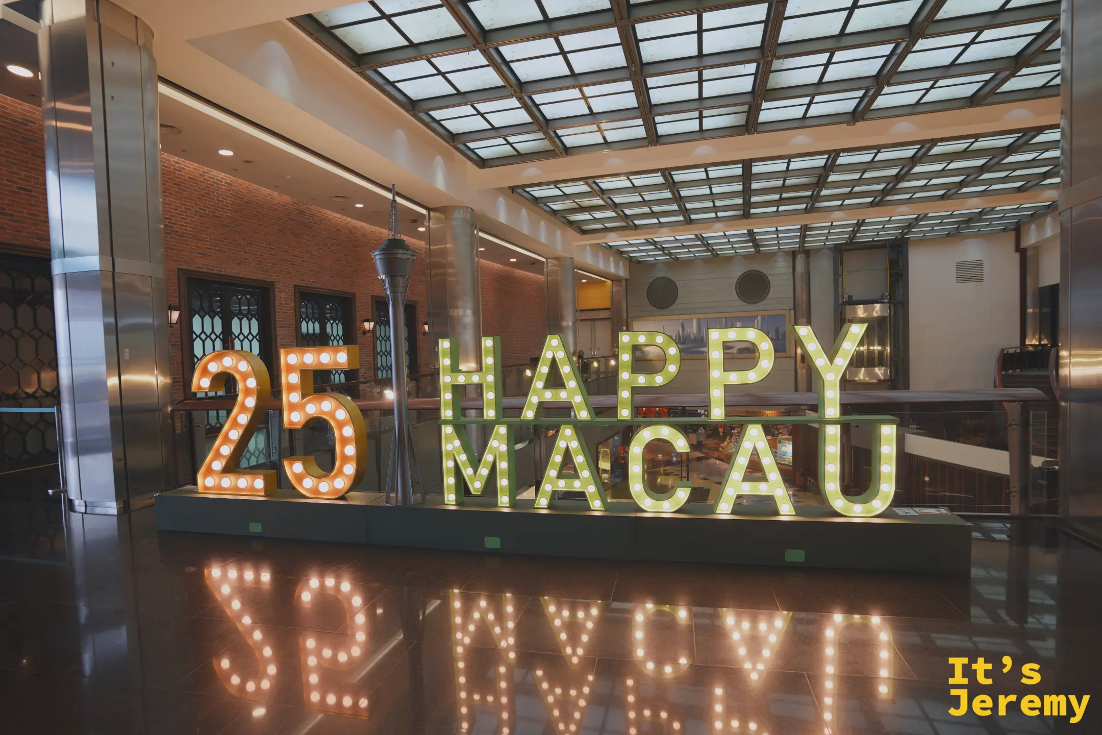澳門塔大廳的 25 HAPPY MACAU 燈牌，旁邊擺著迷你澳門塔模型，燈光倒映在地面