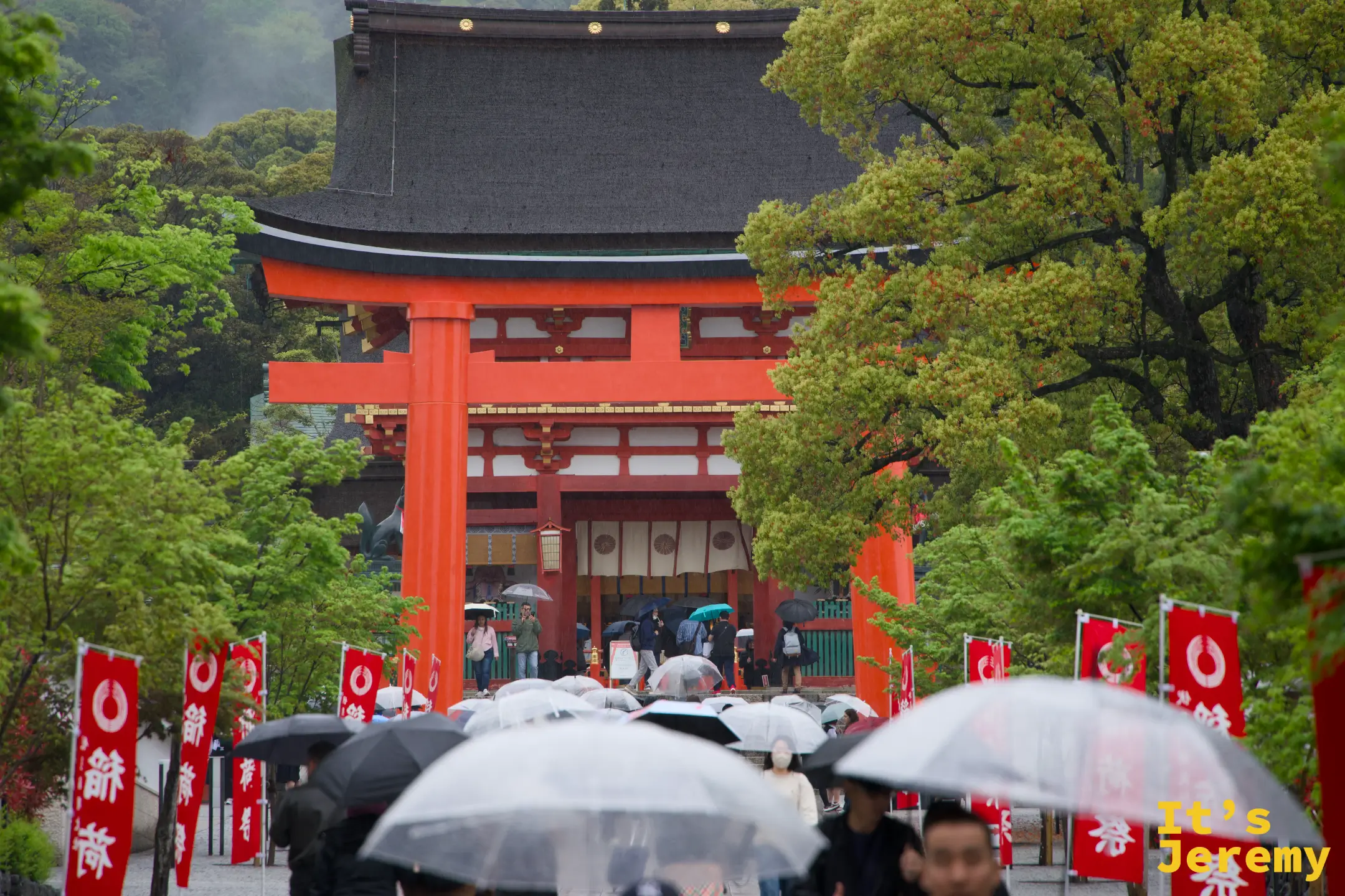 遠景的樓門、鳥居與旗幟，雨中人潮從遠處走來，整個畫面像一張舊明信片