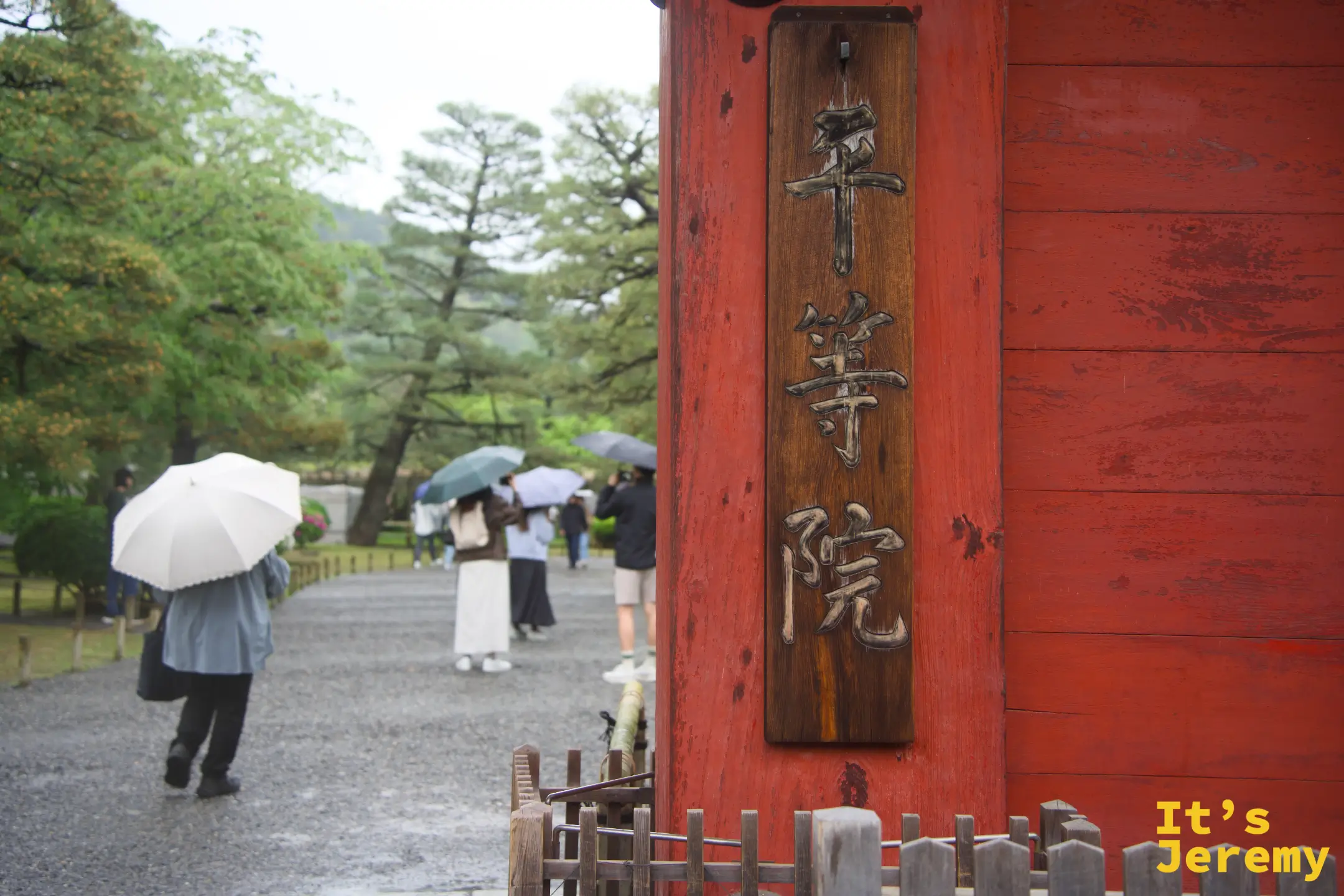 平等院入口的朱紅色大門與「平等院」木牌，雨中訪客各撐著傘魚貫而入