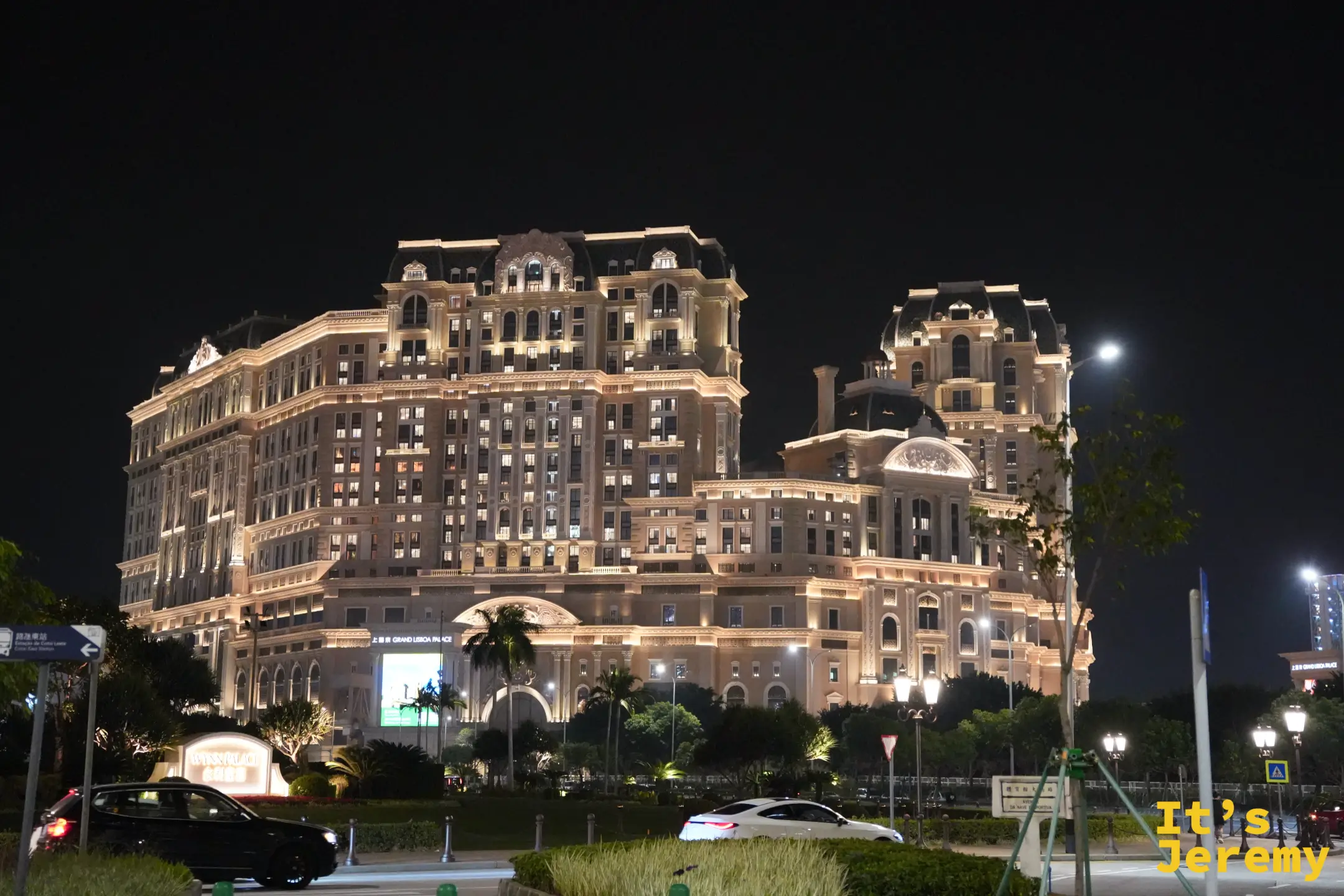 上葡京夜間外觀，金光打亮的歐式宮殿建築，圓頂與雕花立面，前方有車輛駛過