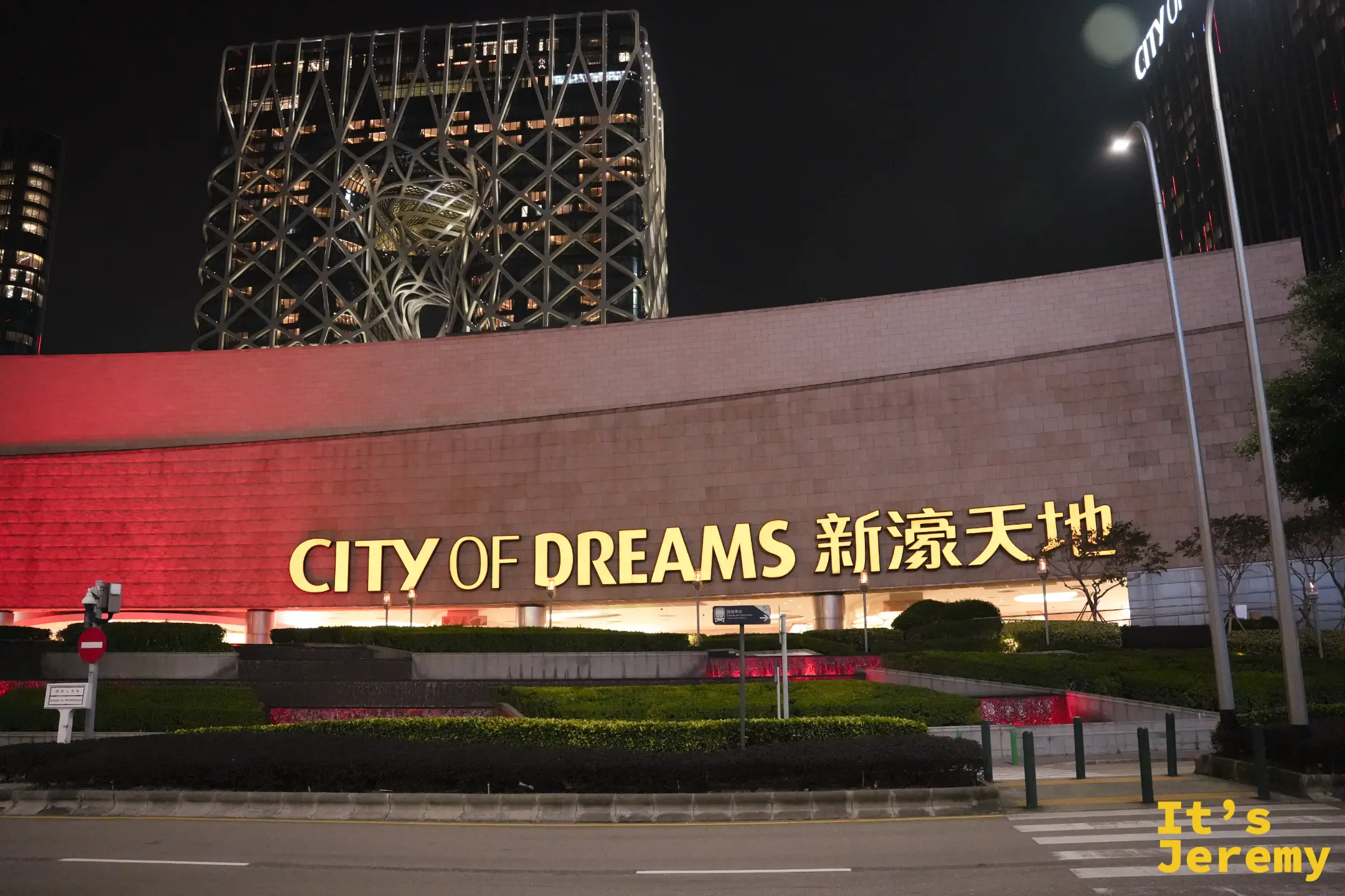 新濠天地夜間外觀，黃色 CITY OF DREAMS 新濠天地招牌，背後是鏤空骨架造型的摩珀斯酒店