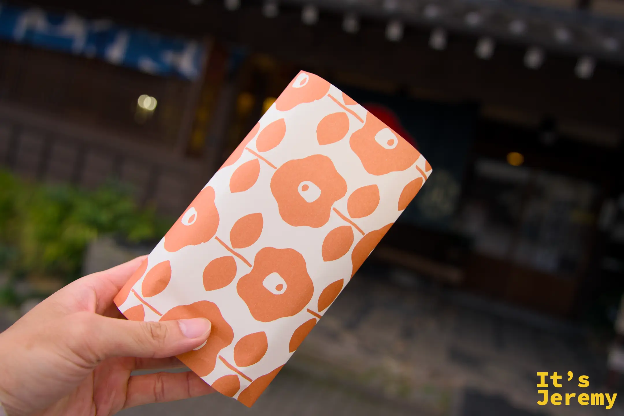 手持人形焼みしまや 橘色印花包裝袋正面，背景是みしまや店鋪