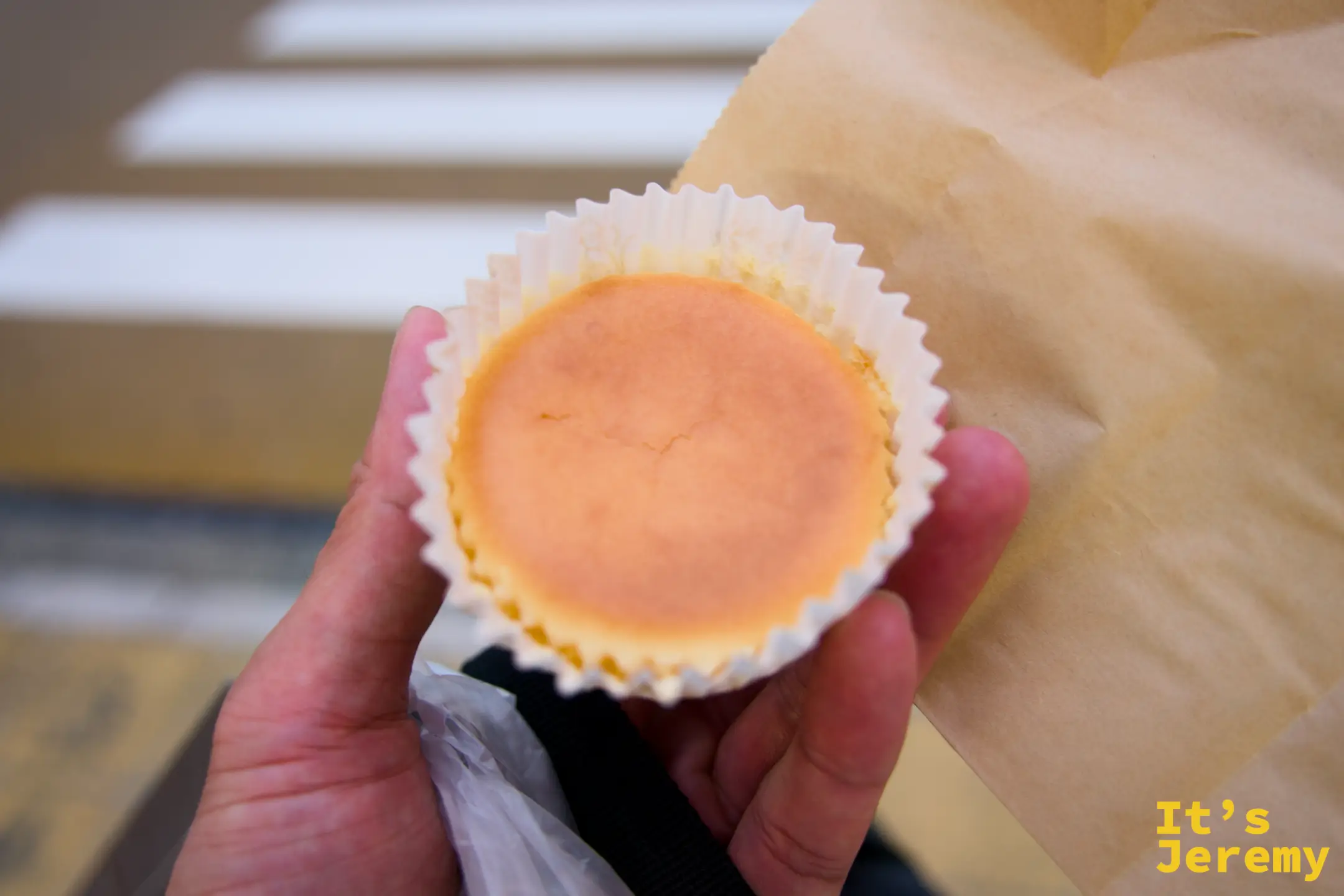 手持日光御用邸ミニチーズケーキ，圓形放在白色紙模中，牛皮紙背景