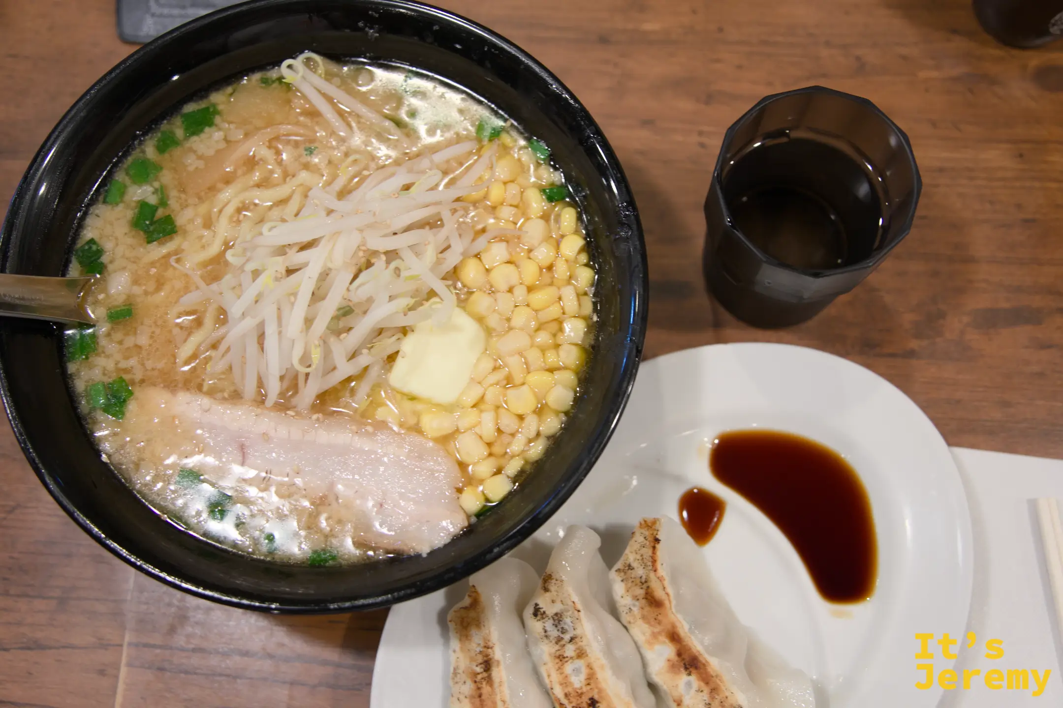 拉麵碗搭配三個餃子的全貌俯拍，餃子在白盤上，旁邊是深色醬汁碟
