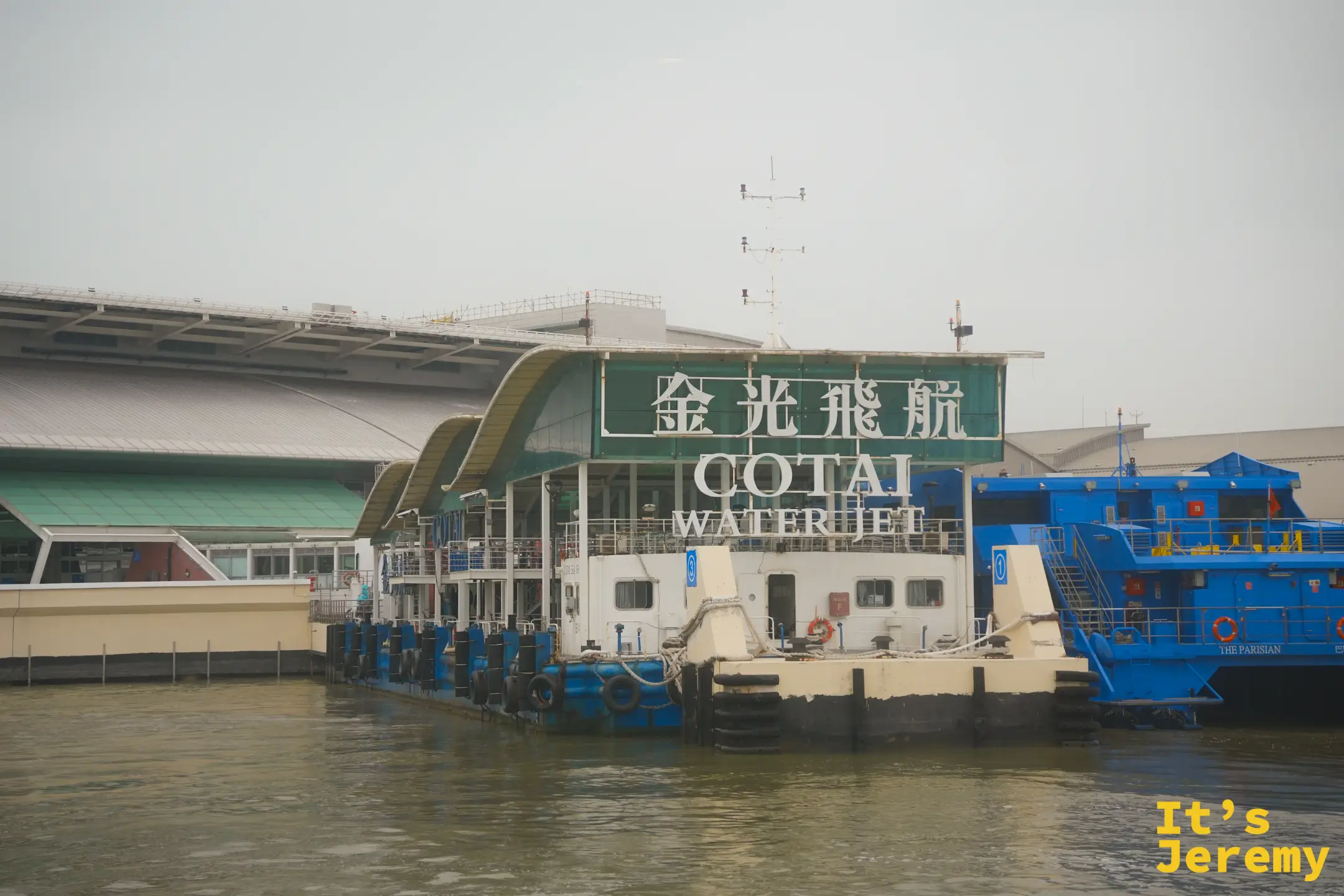 氹仔碼頭綠色玻璃頂的金光飛航候船樓，一旁泊著一艘藍色快船