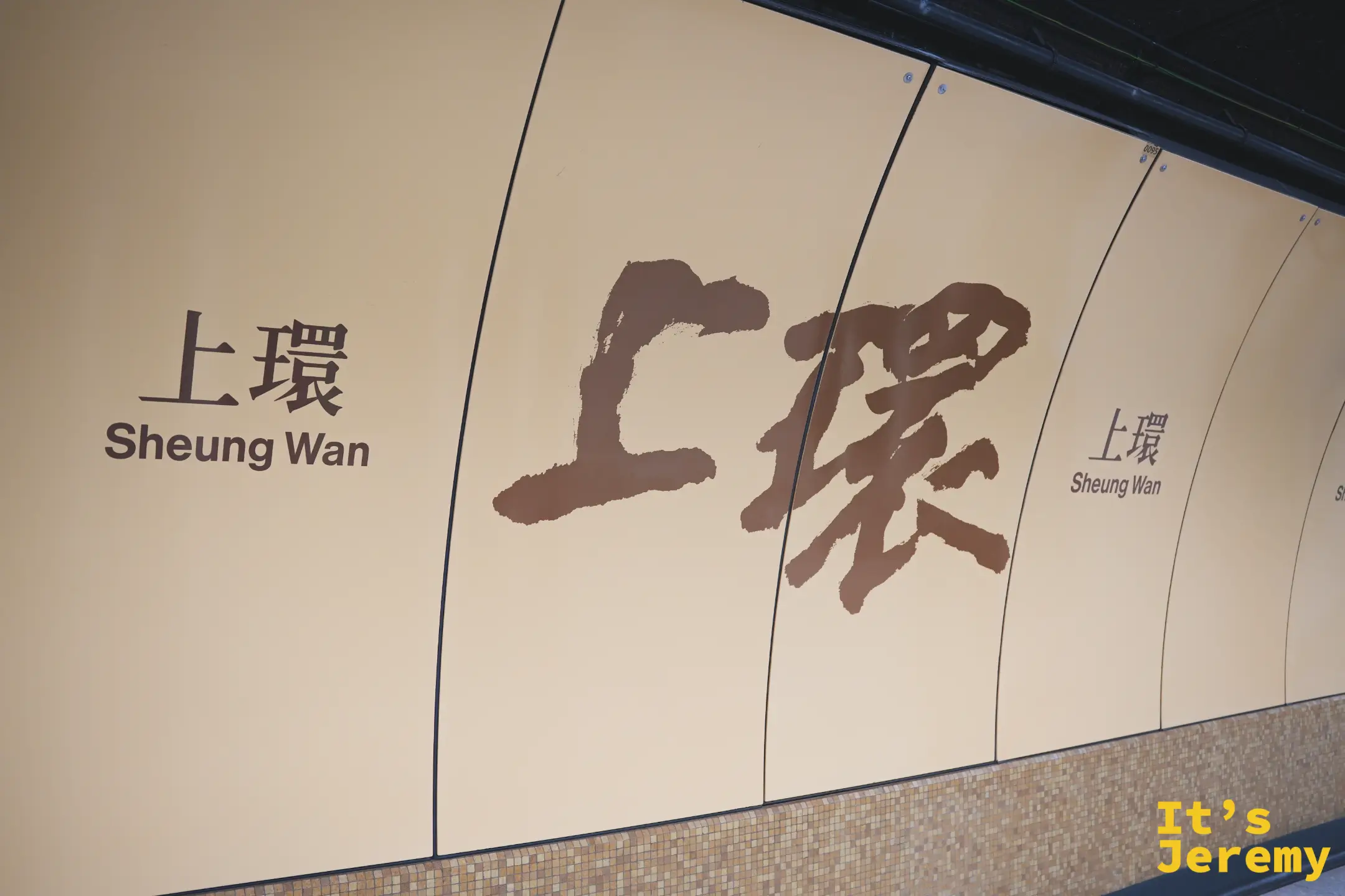 港鐵上環站牆面的書法站名，米色底配咖啡色毛筆字「上環 Sheung Wan」，下方鑲著馬賽克磁磚