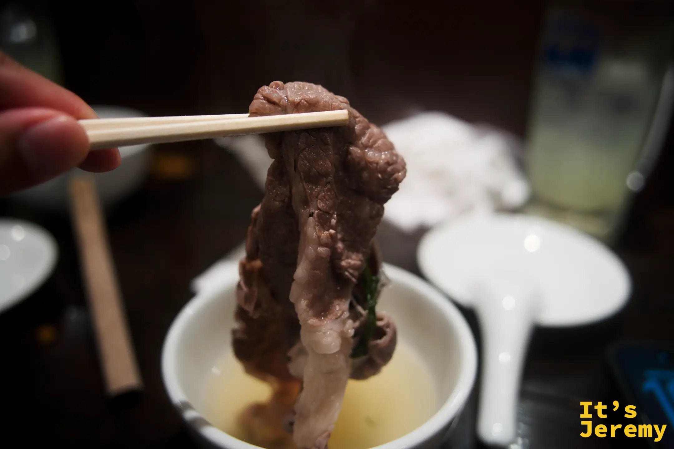 用筷子夾起涮好的和牛，從清澈的柚子高湯中取出