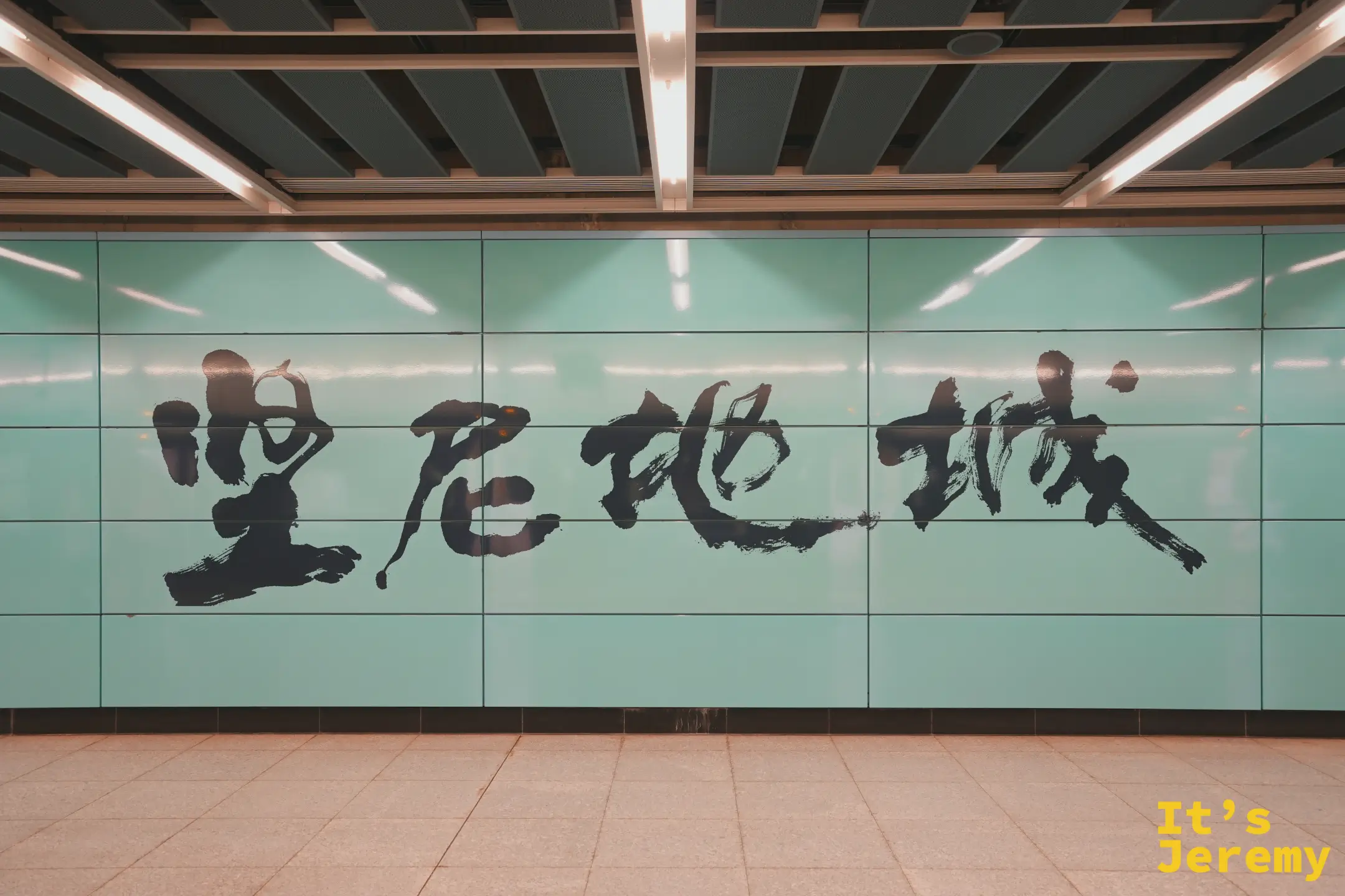 港鐵堅尼地城站月台牆上的書法站名，淡綠底色配黑色毛筆字「堅尼地城 Kennedy Town」