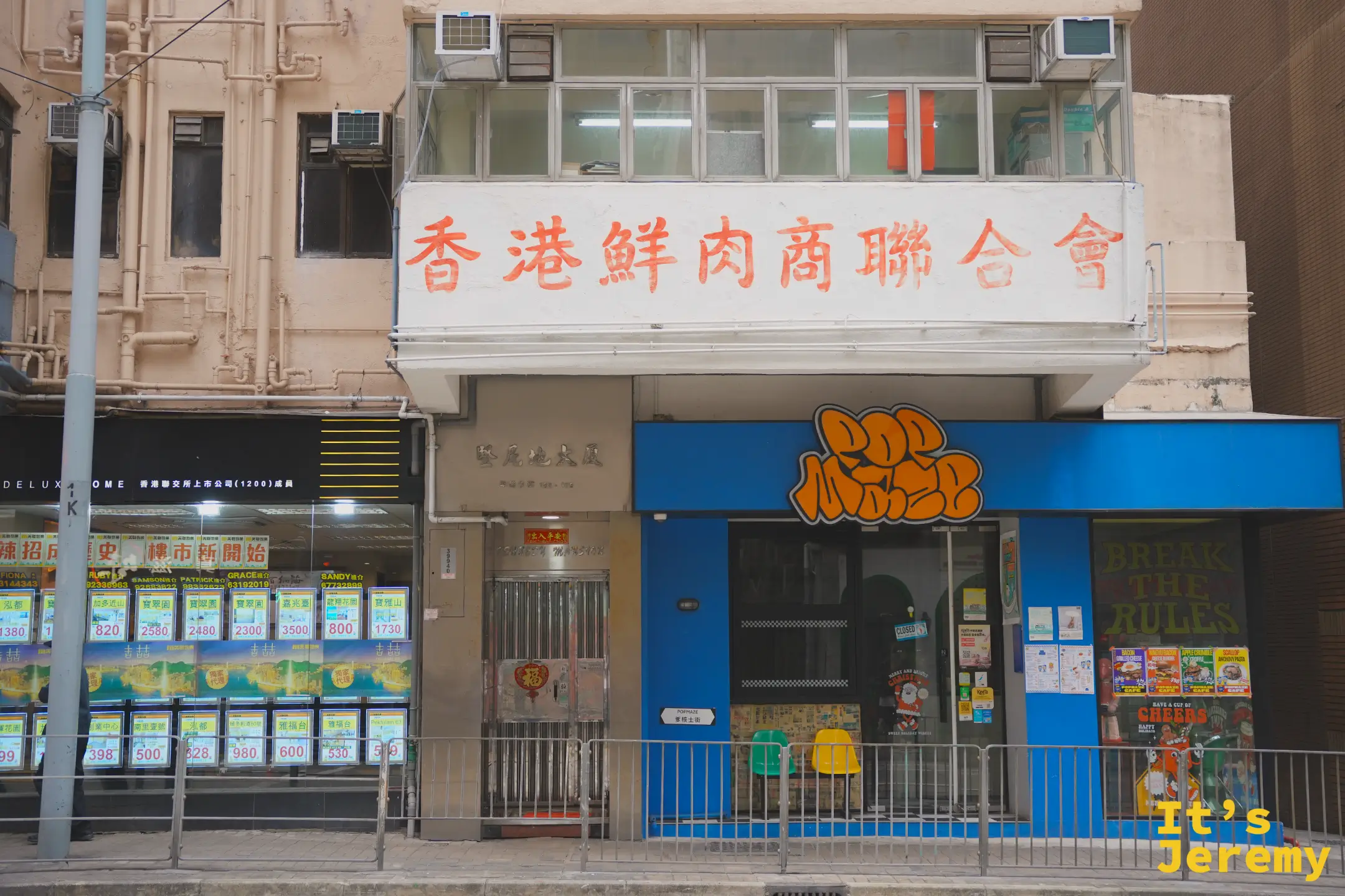 堅尼地城街邊立面，二樓掛著紅字「香港鮮肉商聯合會」招牌，樓下是塗鴉風格的藍色小店與貼滿房價的地產鋪