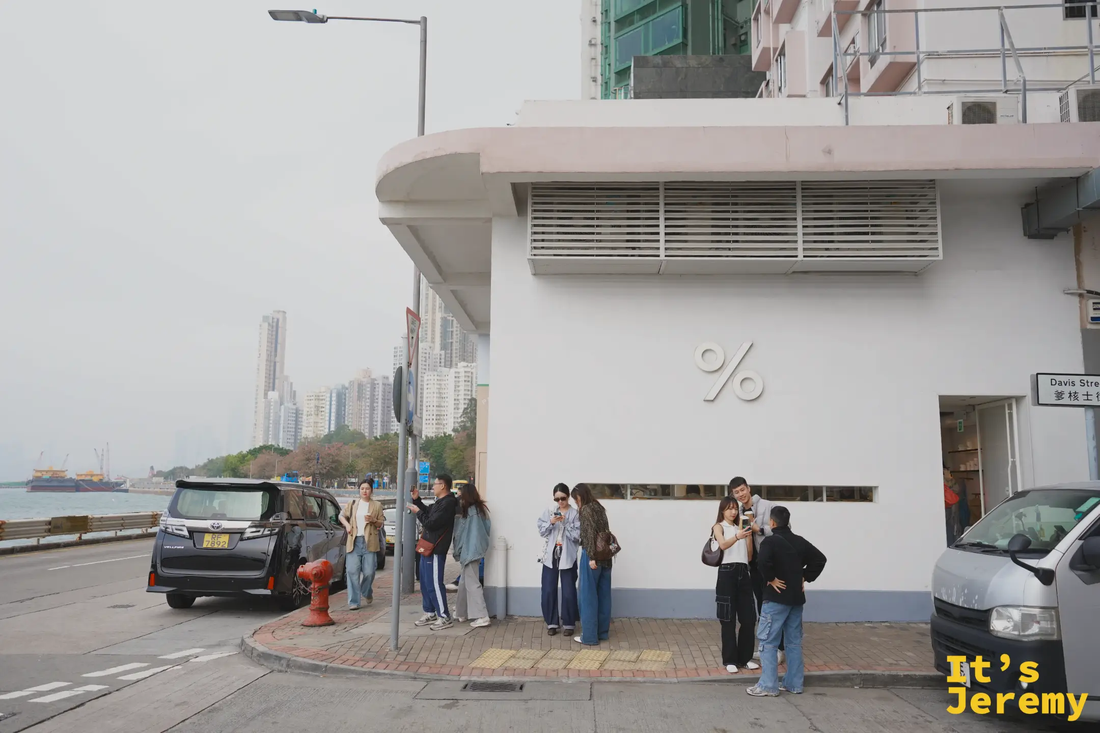 %Arabica 堅尼地城店的白色轉角外牆，牆上掛著立體的白色「%」logo，一群年輕人拿著咖啡在門口拍照