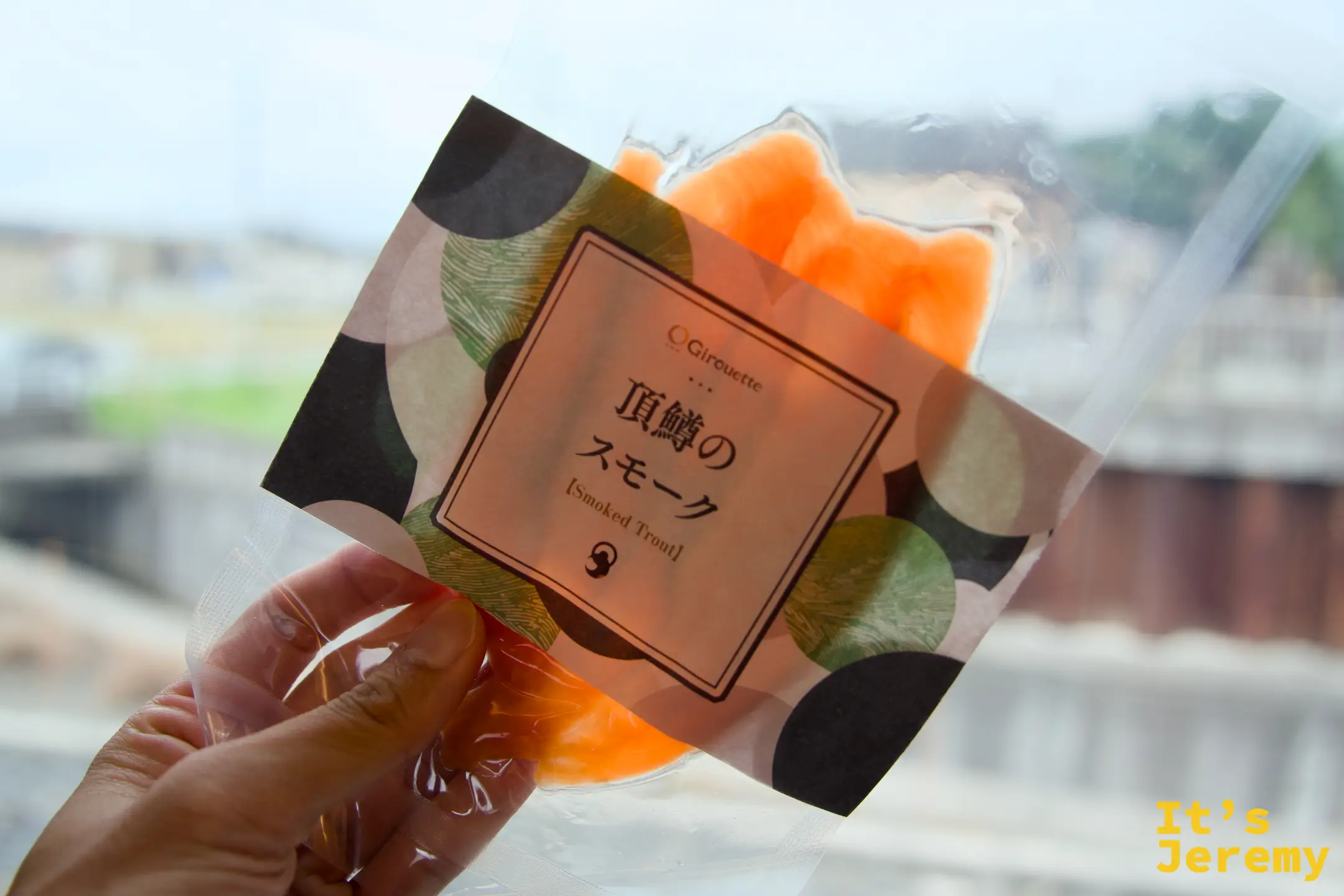 手持頂鱒のスモーク（Smoked Trout）包裝正面，橘色燻製魚片透過透明包裝可見