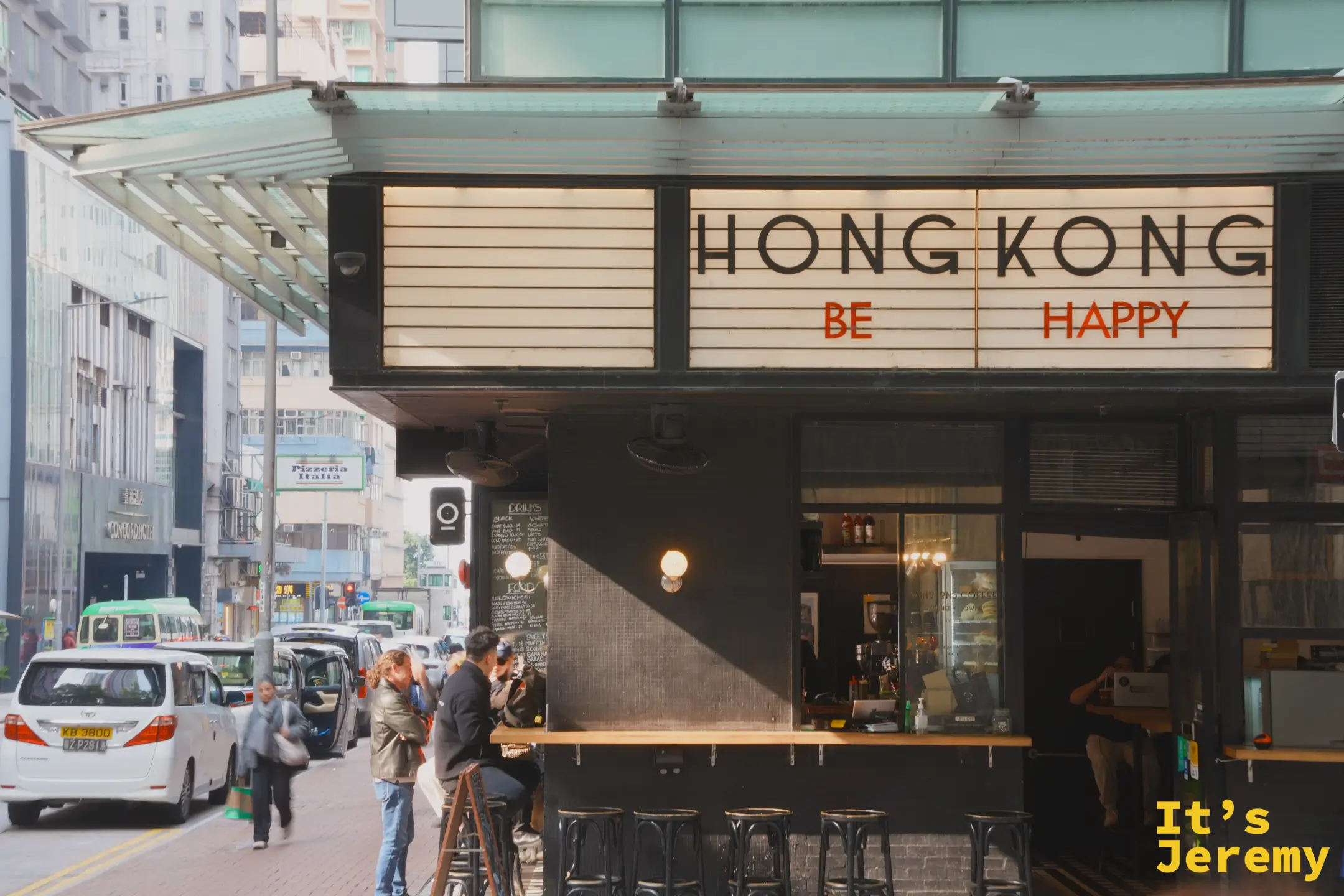 WINSTONS COFFEE 另一面的黑色招牌寫著 HONG KONG BE HAPPY，木製吧台對著馬路，客人站著坐著喝咖啡