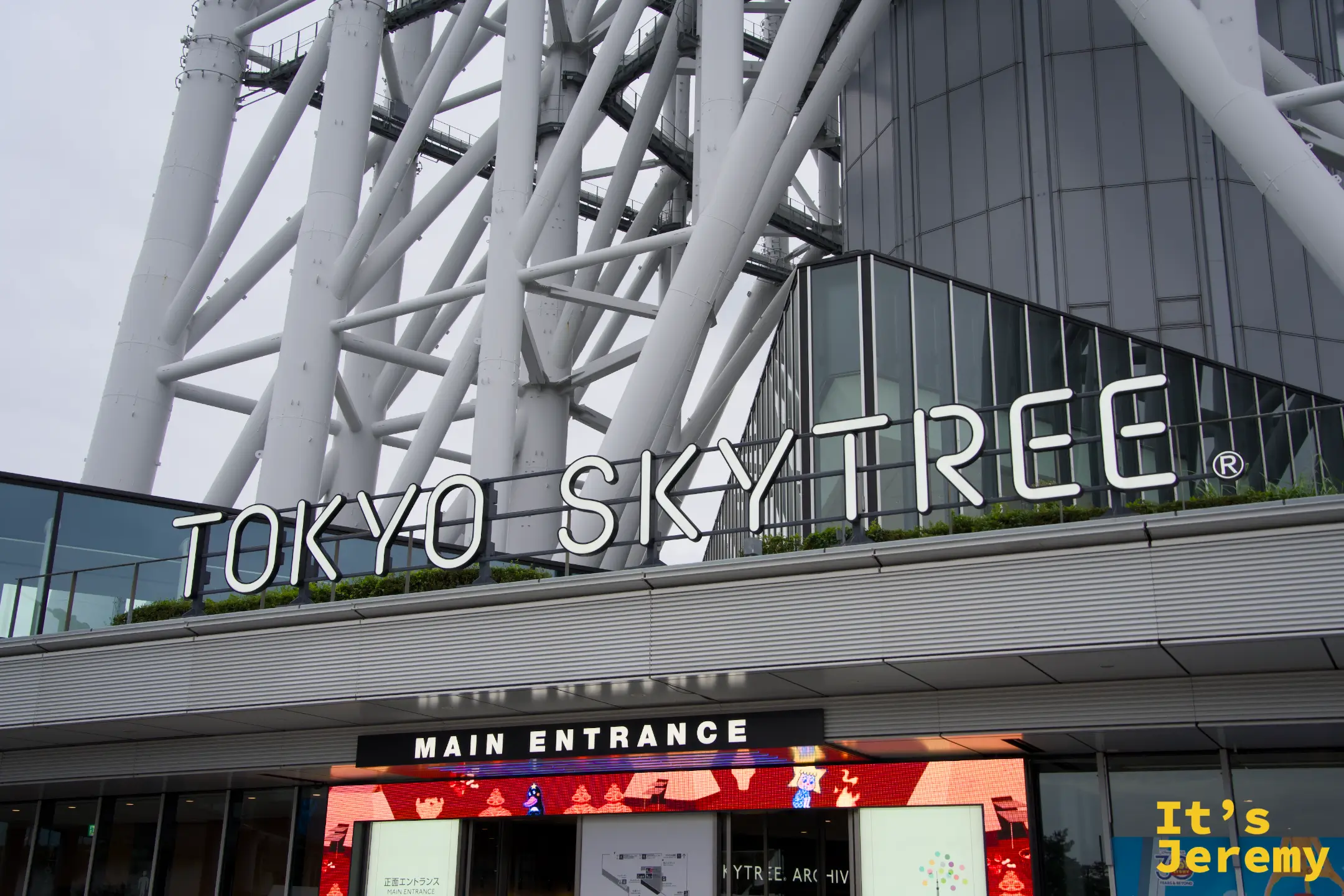 Tokyo Skytree® Main Entrance 正面入口,白色大字招牌在玻璃帷幕後方,Toy Story 等合作廣告可見