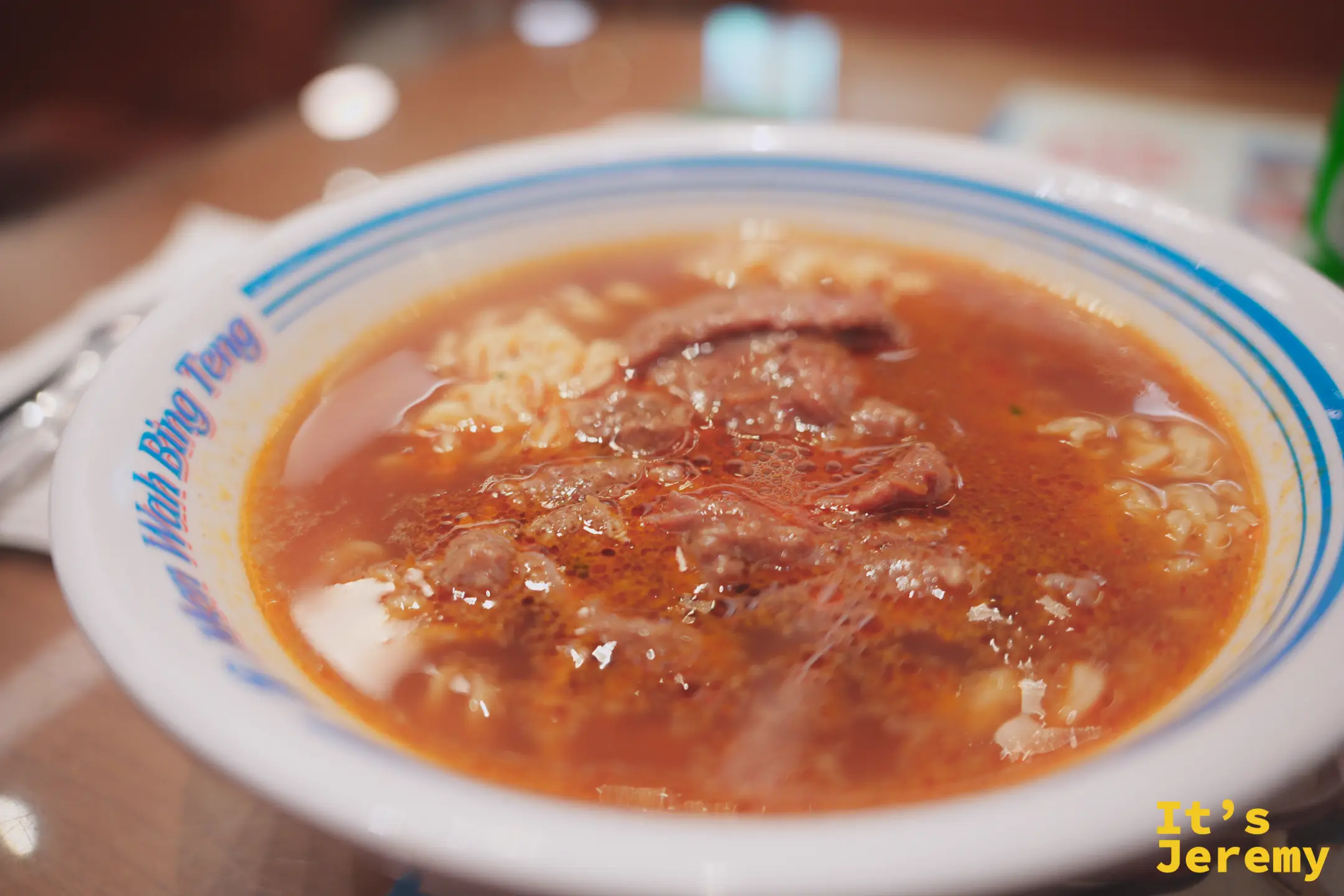 印著「Wah Bing Teng」的白瓷碗裝著潮式沙茶牛肉公仔麵，紅澄澄的沙茶湯底裡有麵條與數片牛肉