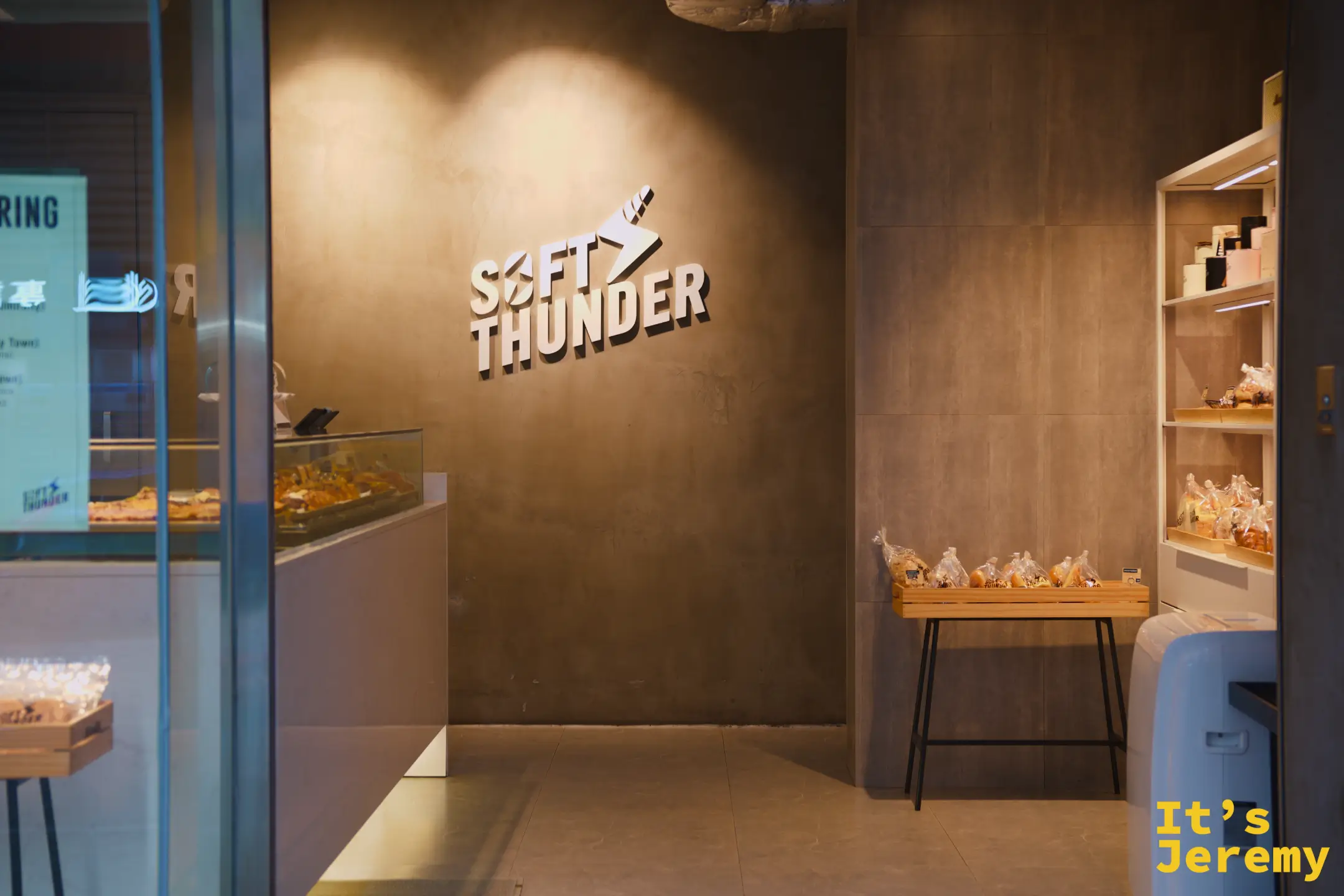 SOFT THUNDER 麵包店室內，清水模牆面打著品牌 logo，木架與檯面上擺著一袋袋用透明袋裝好的麵包