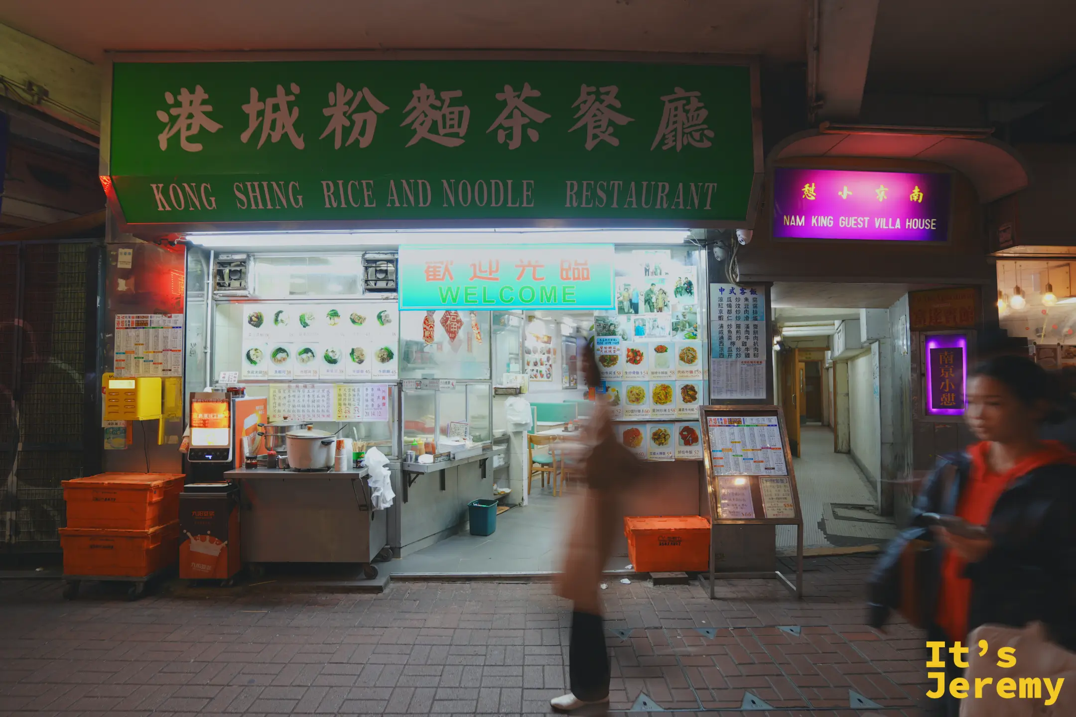 港城粉麵茶餐廳的綠底金字招牌「港城粉麵茶餐廳 KONG SHING RICE AND NOODLE RESTAURANT」，下方是開放式檔口與煮麵大鍋，牆上貼滿菜單，一名客人走過
