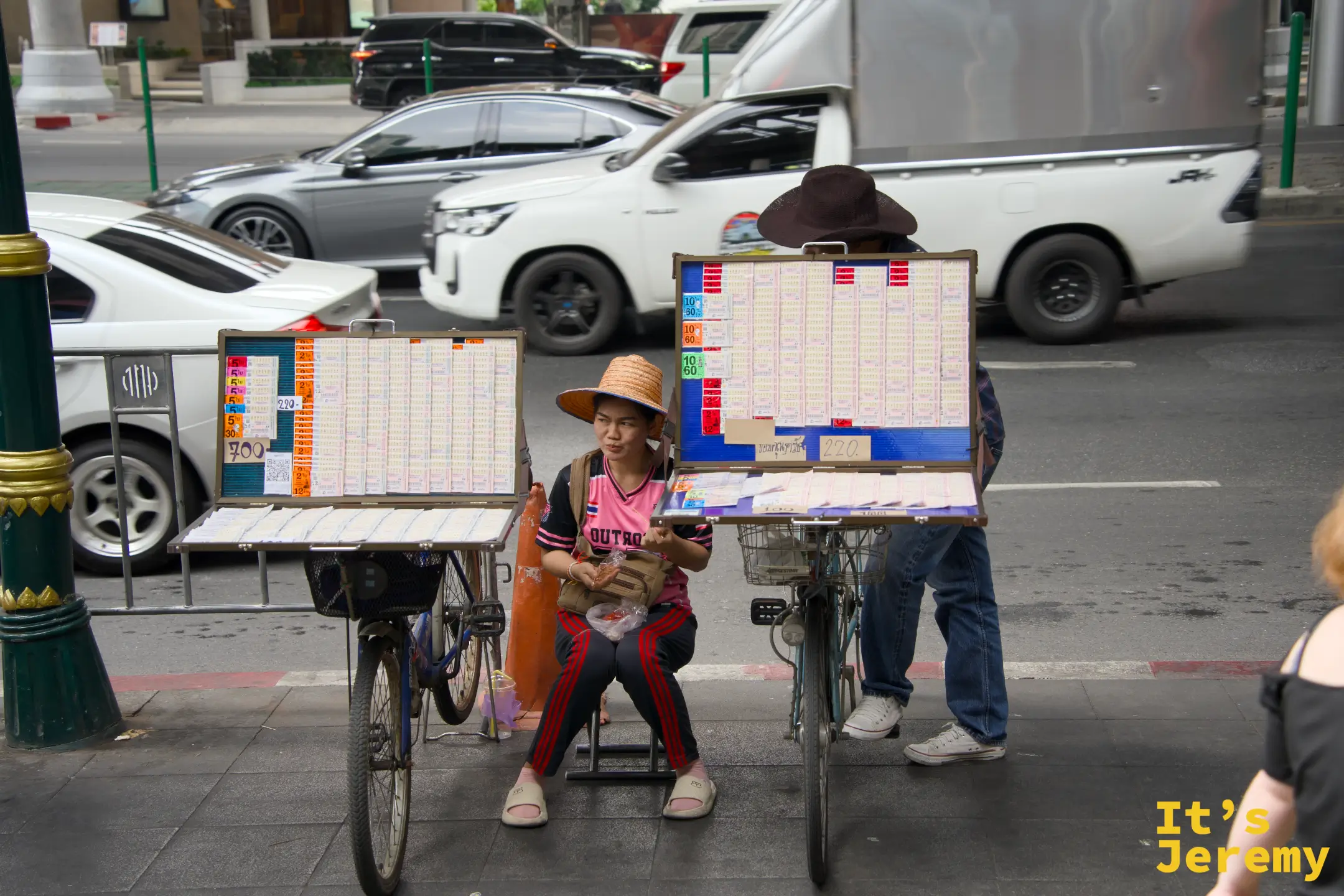 路邊的彩券小販騎著腳踏車，車籃裡夾著一排彩券，吞武里街頭日常