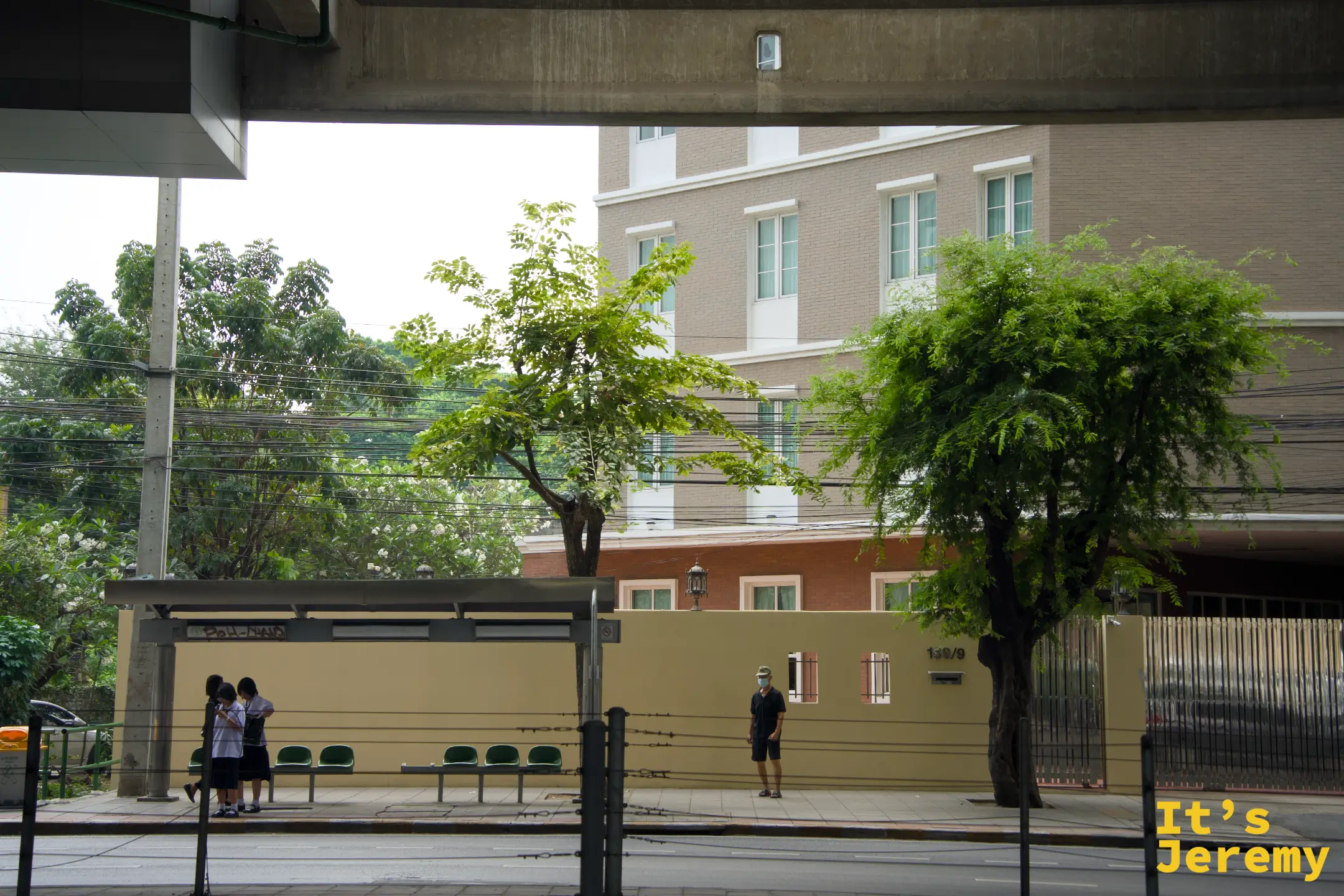 MRT Bang Phai 站附近的公車站，幾名學生在高架捷運橋下等車，陽光還沒曬進來