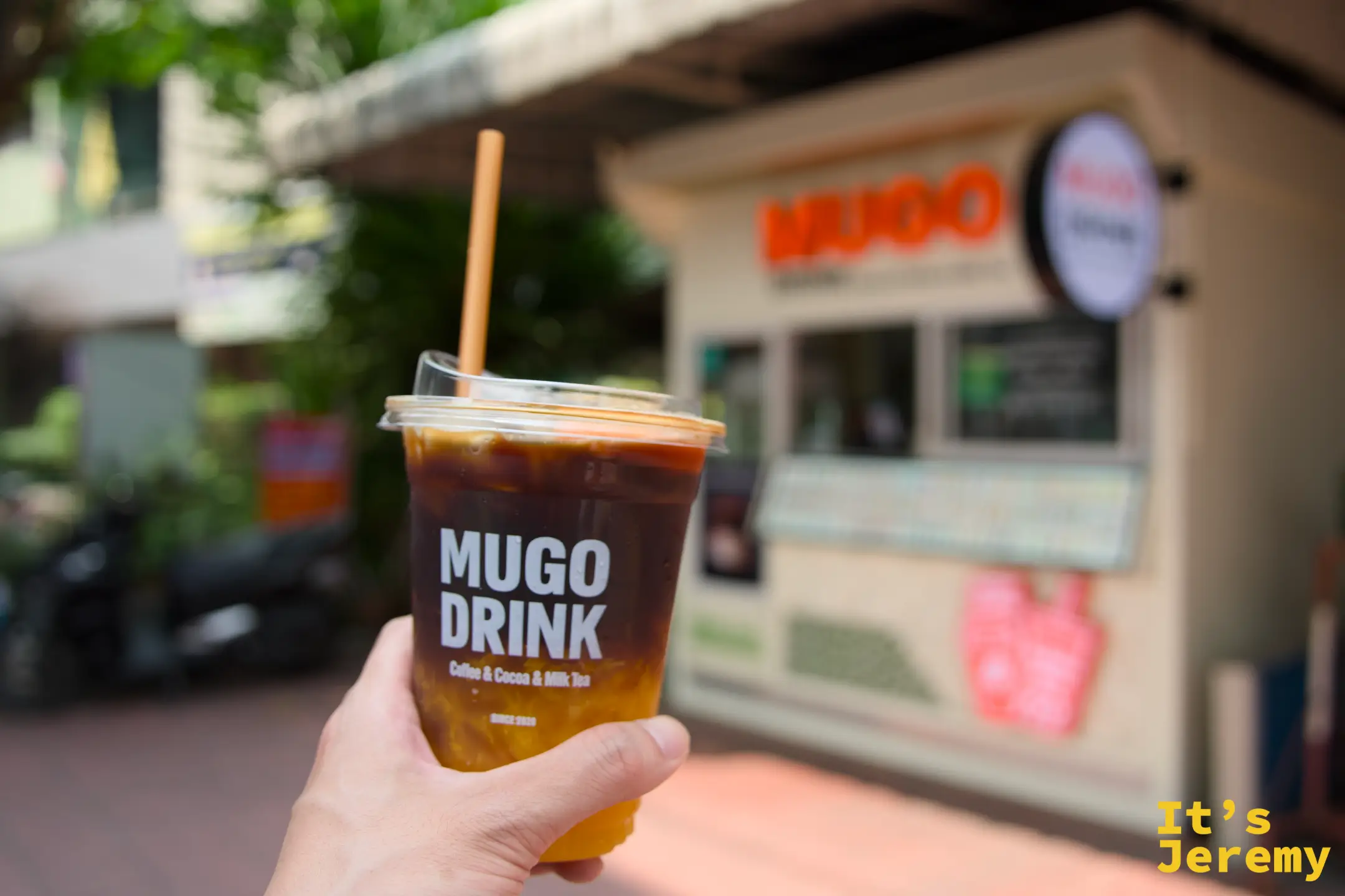 手持 MUGO Drink Orange Americano，橙汁切開咖啡的厚度，是頂著大太陽走吞武里的續命飲料
