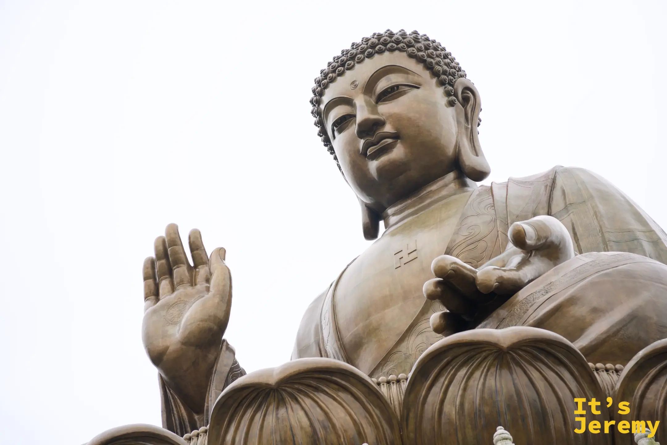 天壇大佛面部與胸前特寫，青銅佛像雙眼低垂、嘴角含笑，右手施無畏印，胸前有卍字，衣袍刻著雲紋