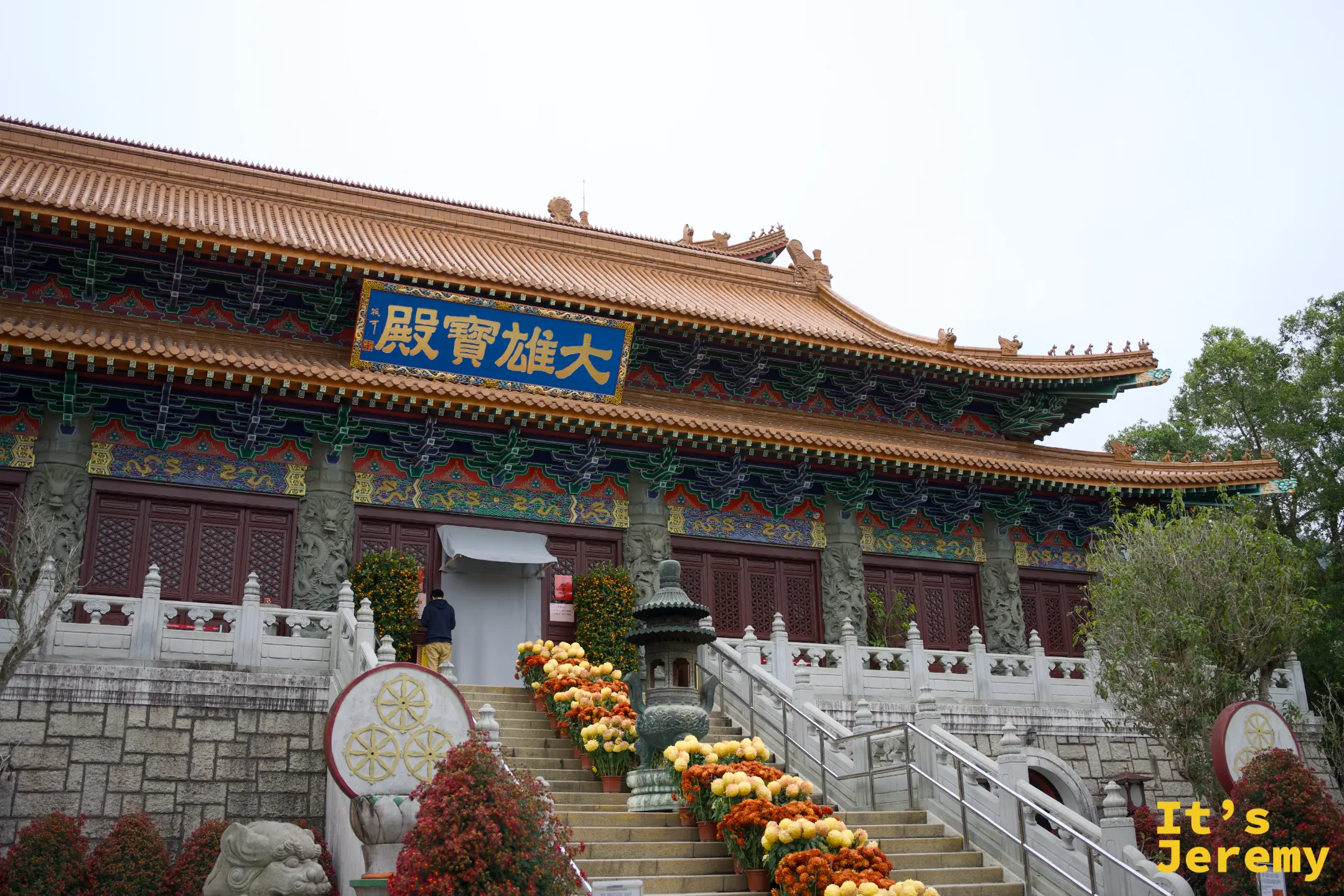 大雄寶殿側前方一景，色彩鮮豔的北方彩繪樑枋、橙紅瓦頂，殿前石階兩旁排滿橘黃菊花與圓形石雕