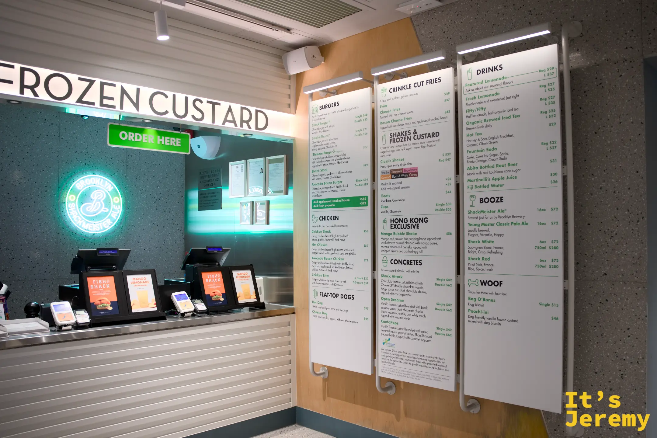 SHAKE SHACK 點餐區，綠色 ORDER HERE 燈牌下方有多台自助點餐機，旁邊是不鏽鋼櫃檯與菜單板