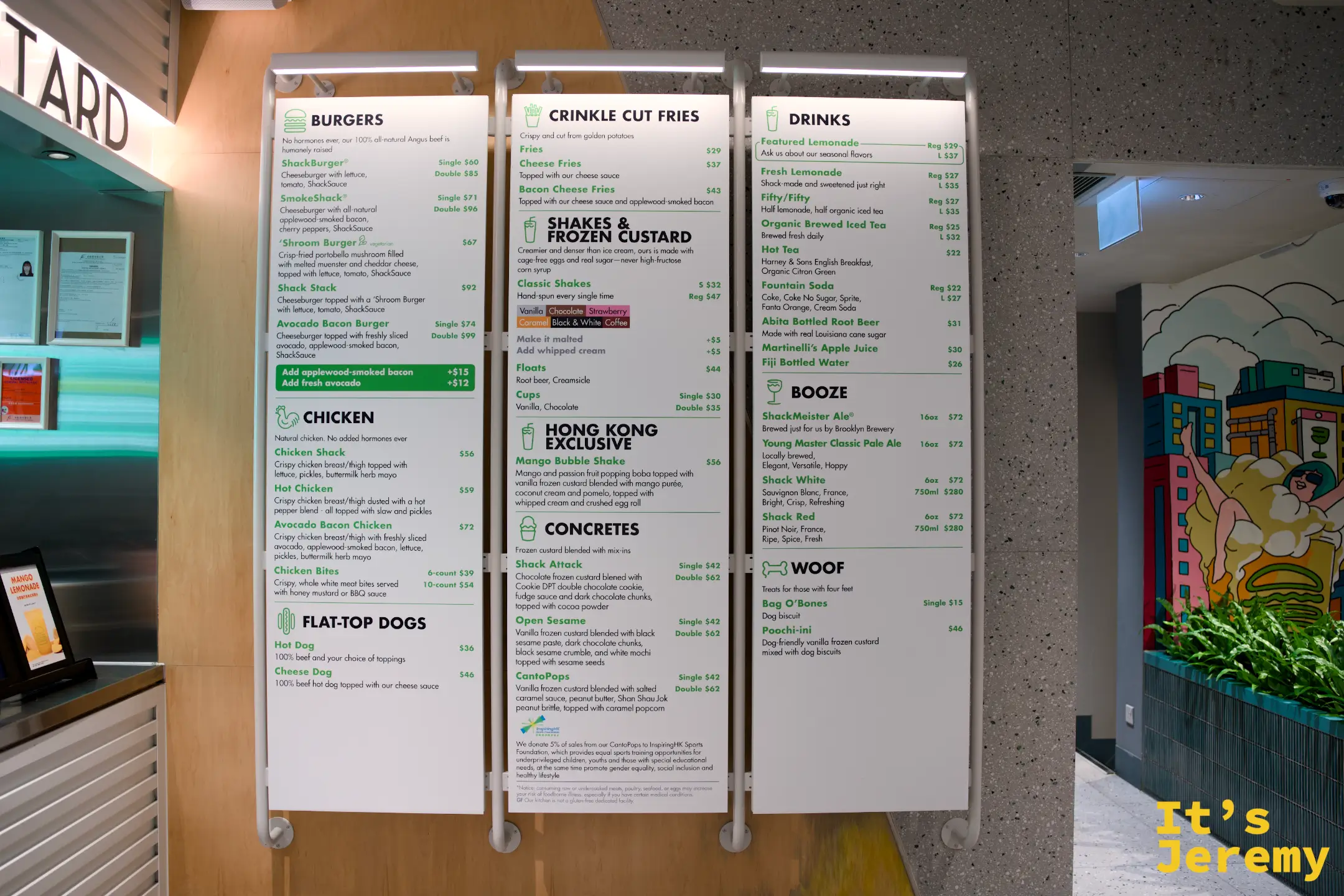 SHAKE SHACK 店內三面直立式菜單板，分別列出 BURGERS、CHICKEN、CRINKLE CUT FRIES、DRINKS 與香港限定的 Mango Bubble Shake 等品項，字體為綠色