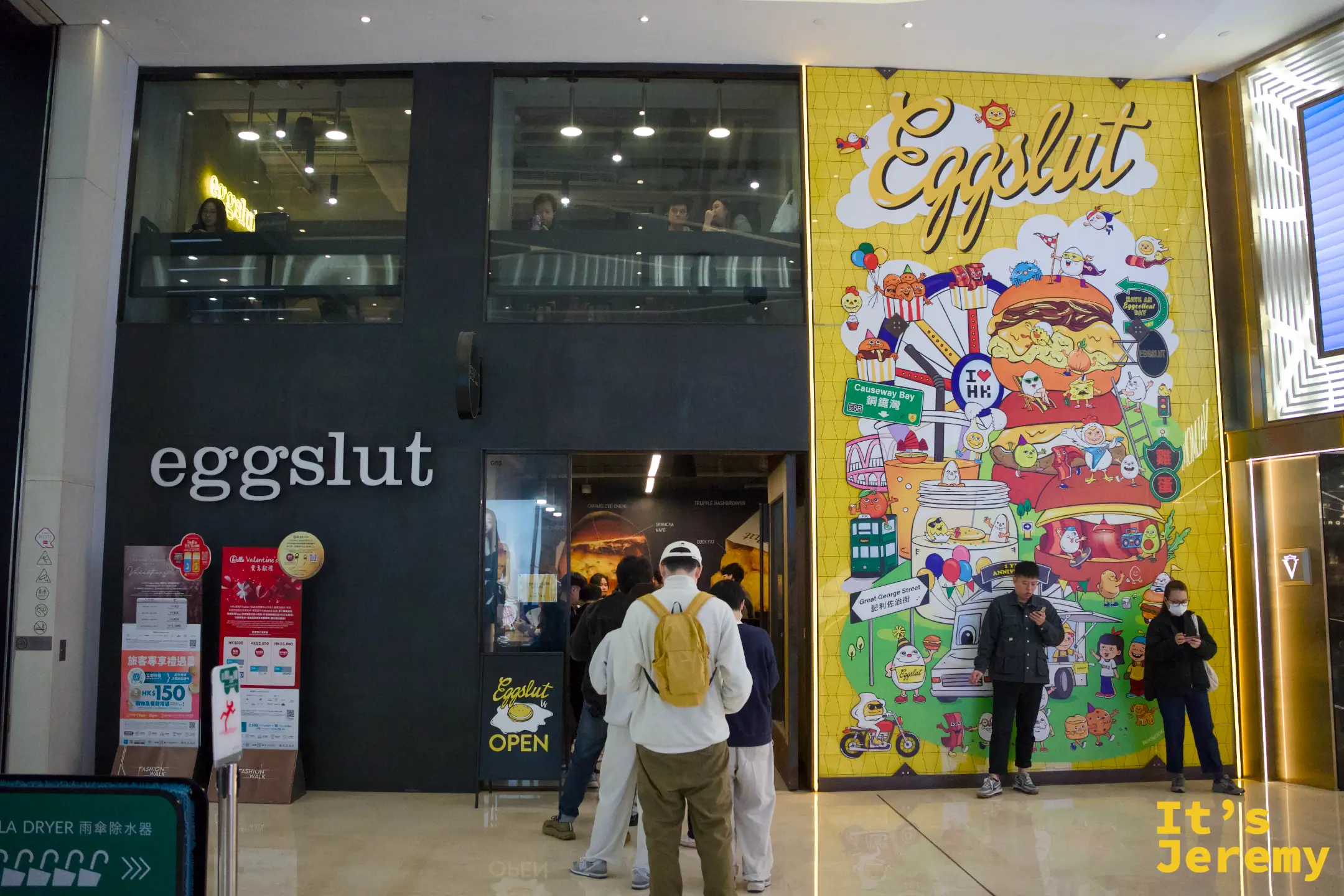 eggslut 立體字招牌特寫，白色「eggslut」字樣旁是一個黃黑相間的圓形 EGGSLUT 標誌，下方貼著活動海報