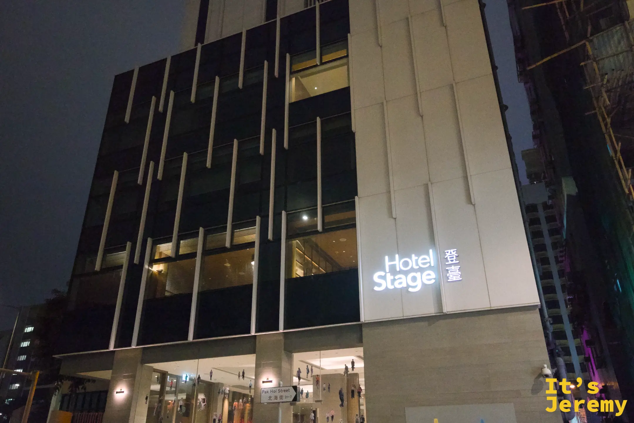 夜裡的登臺 Hotel Stage 建築立面，深色外牆嵌著一排排直立燈條，右側亮著白色「Hotel Stage 登臺」招牌，樓下是明亮的大廳入口