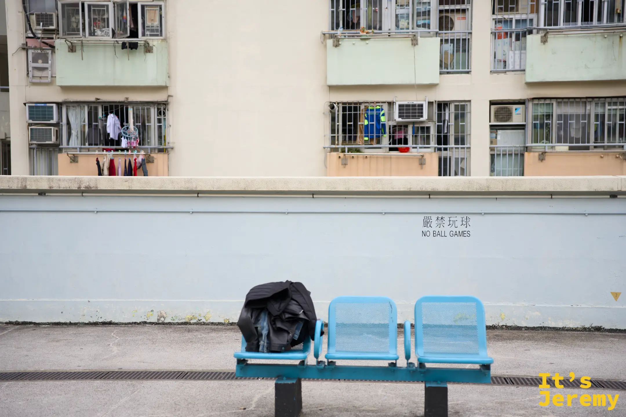 三張藍色座椅並排，其中一張放著外套，後方矮牆上寫著「嚴禁玩球 NO BALL GAMES」