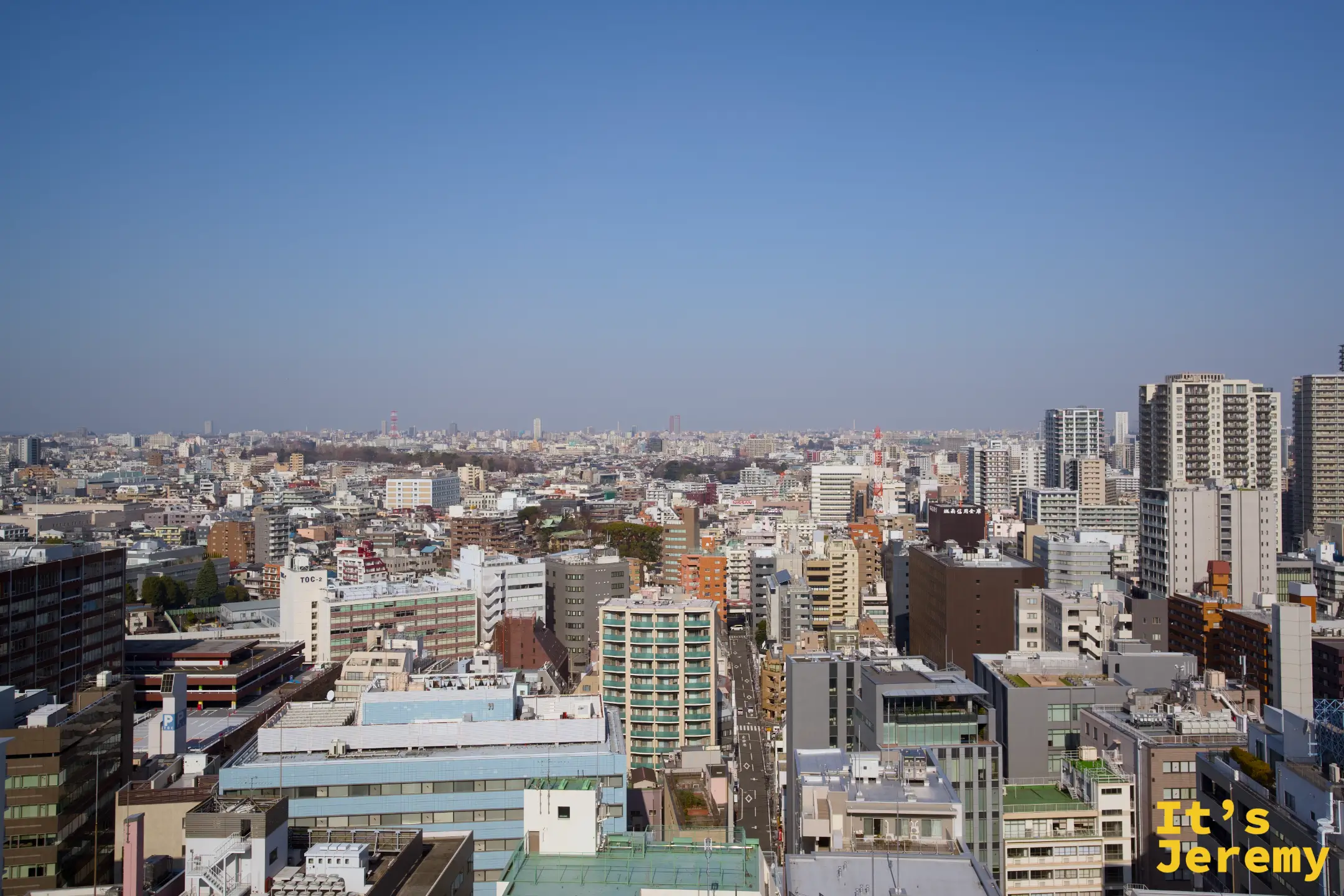 從東京高處俯瞰城市天際線，密集的大樓建築一直延伸到地平線盡頭，天空湛藍無雲