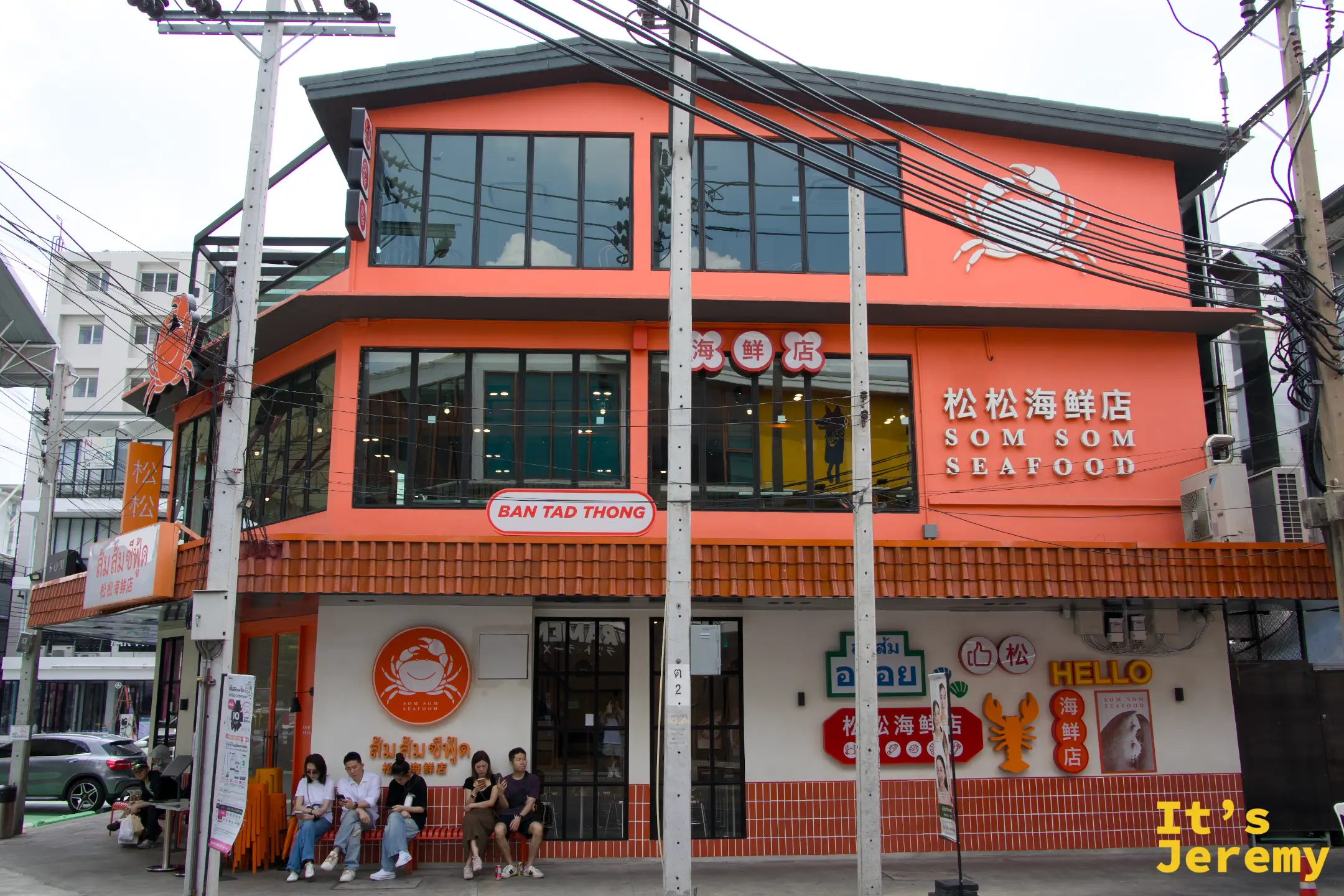 松松海鮮三層樓高的橘色店面外觀，樓下有顧客坐在長椅上候位