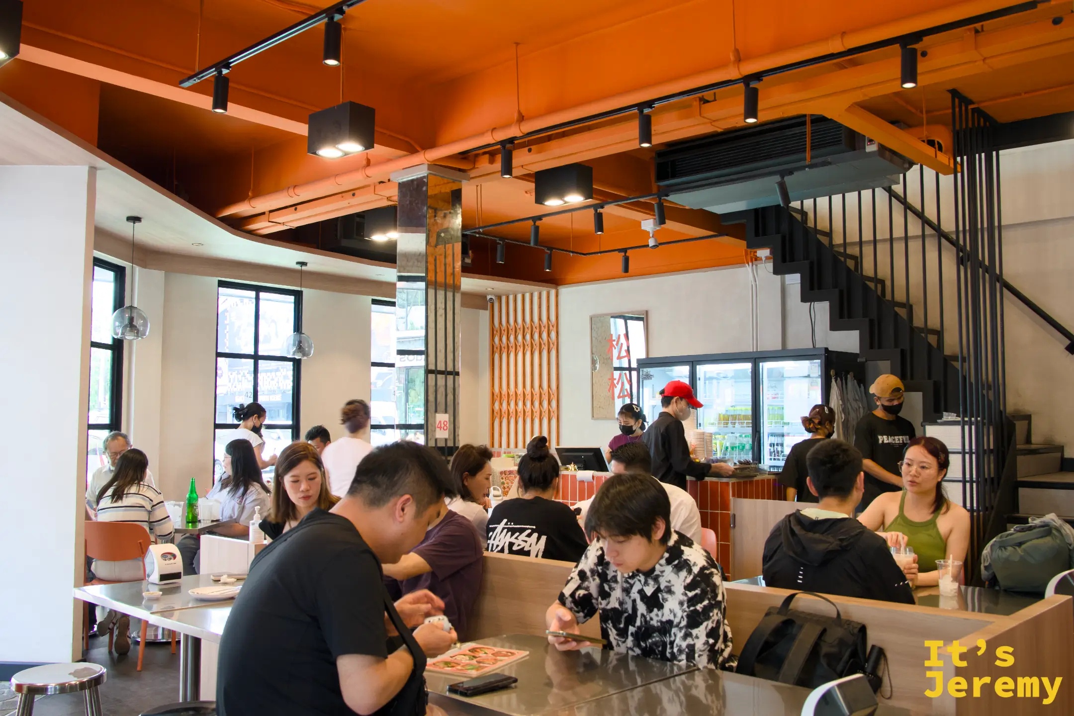 店內用餐區，工業風裸露天花板、黑色鐵梯與多桌用餐的客人