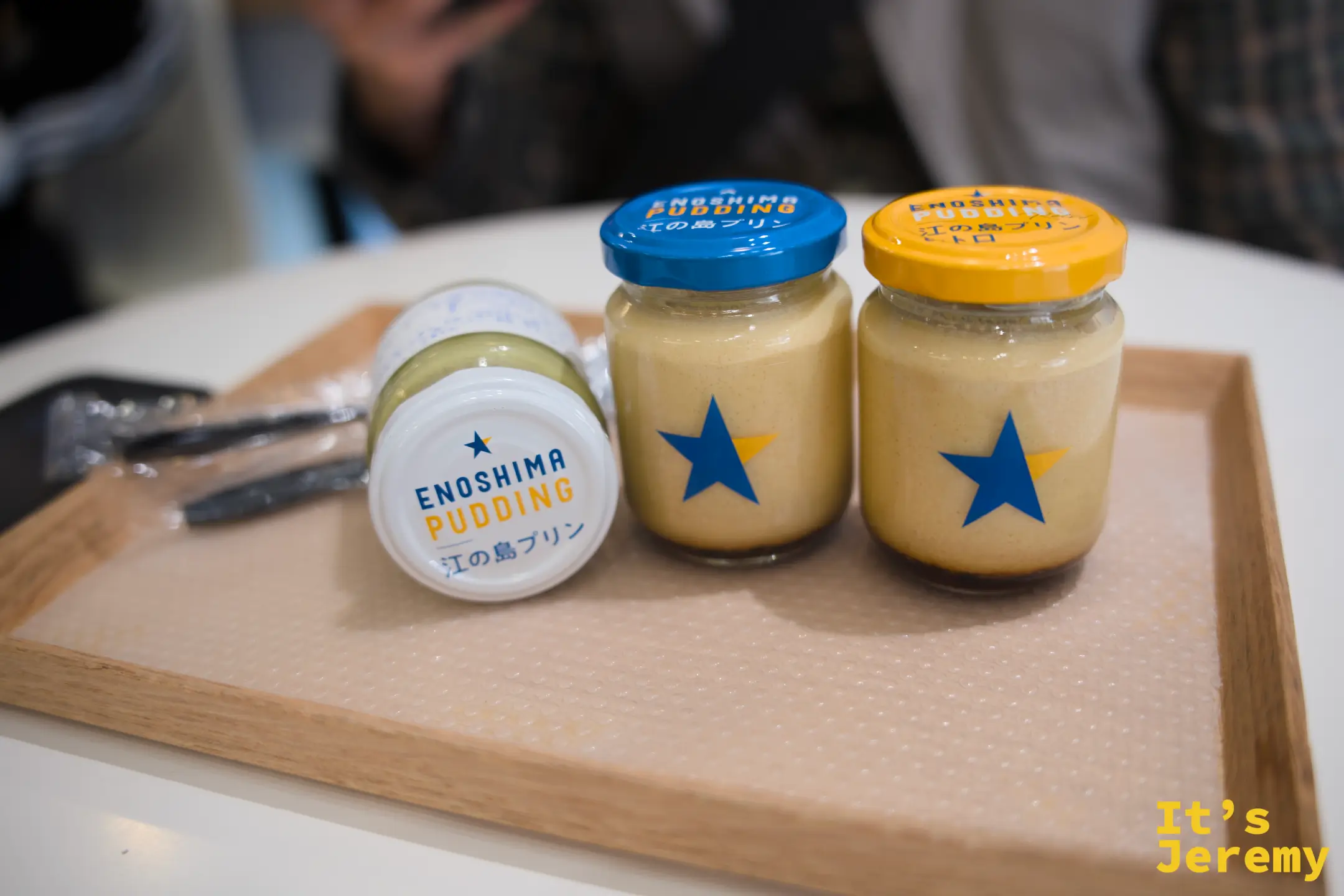 其中一瓶江の島プリン側躺展示，瓶身正面清楚可見「ENOSHIMA PUDDING 江の島プリン」英日文字樣