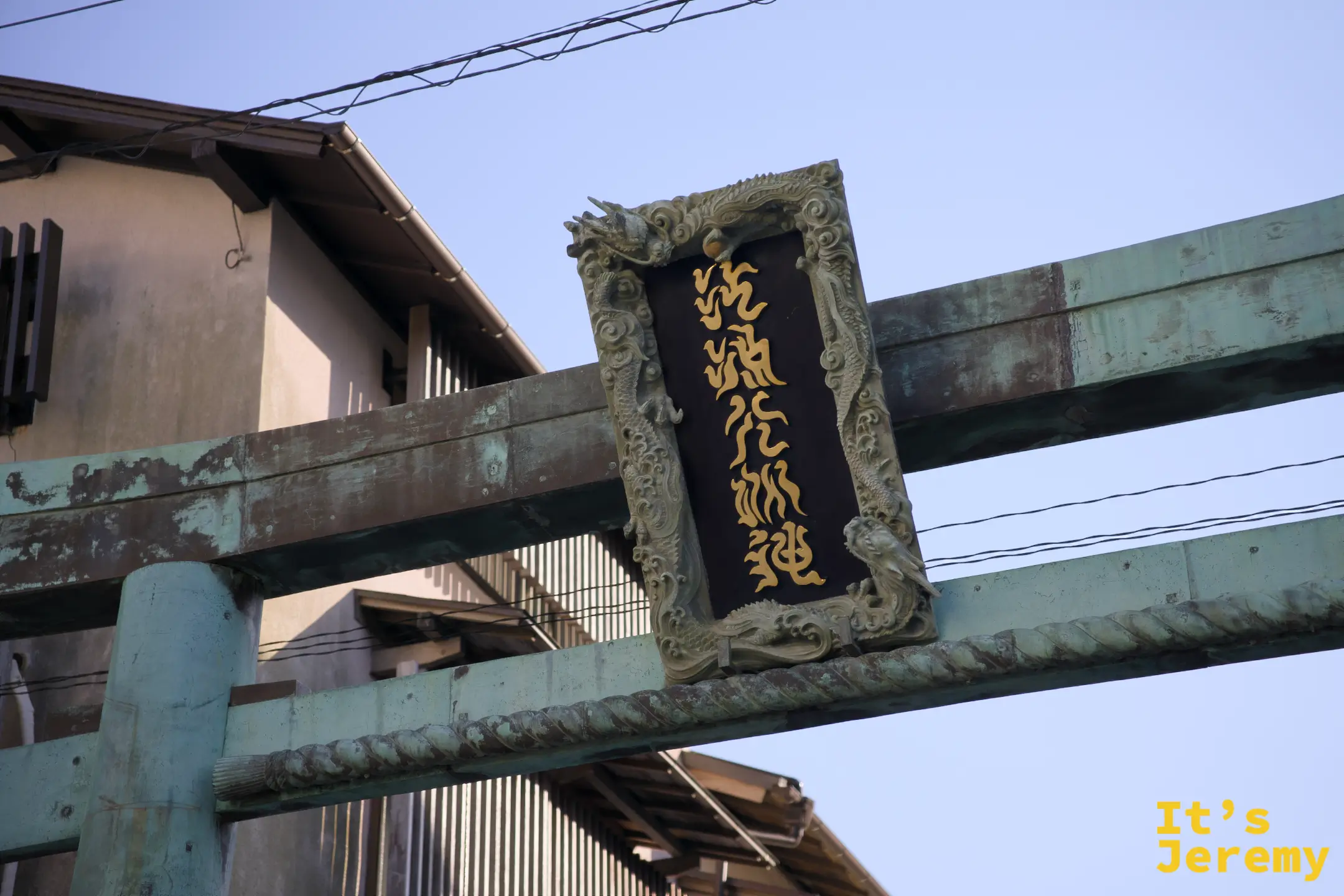 銅鳥居橫樑上飾有龍紋邊框的「江島神社」金字匾額，青銅表面已自然氧化成青綠色