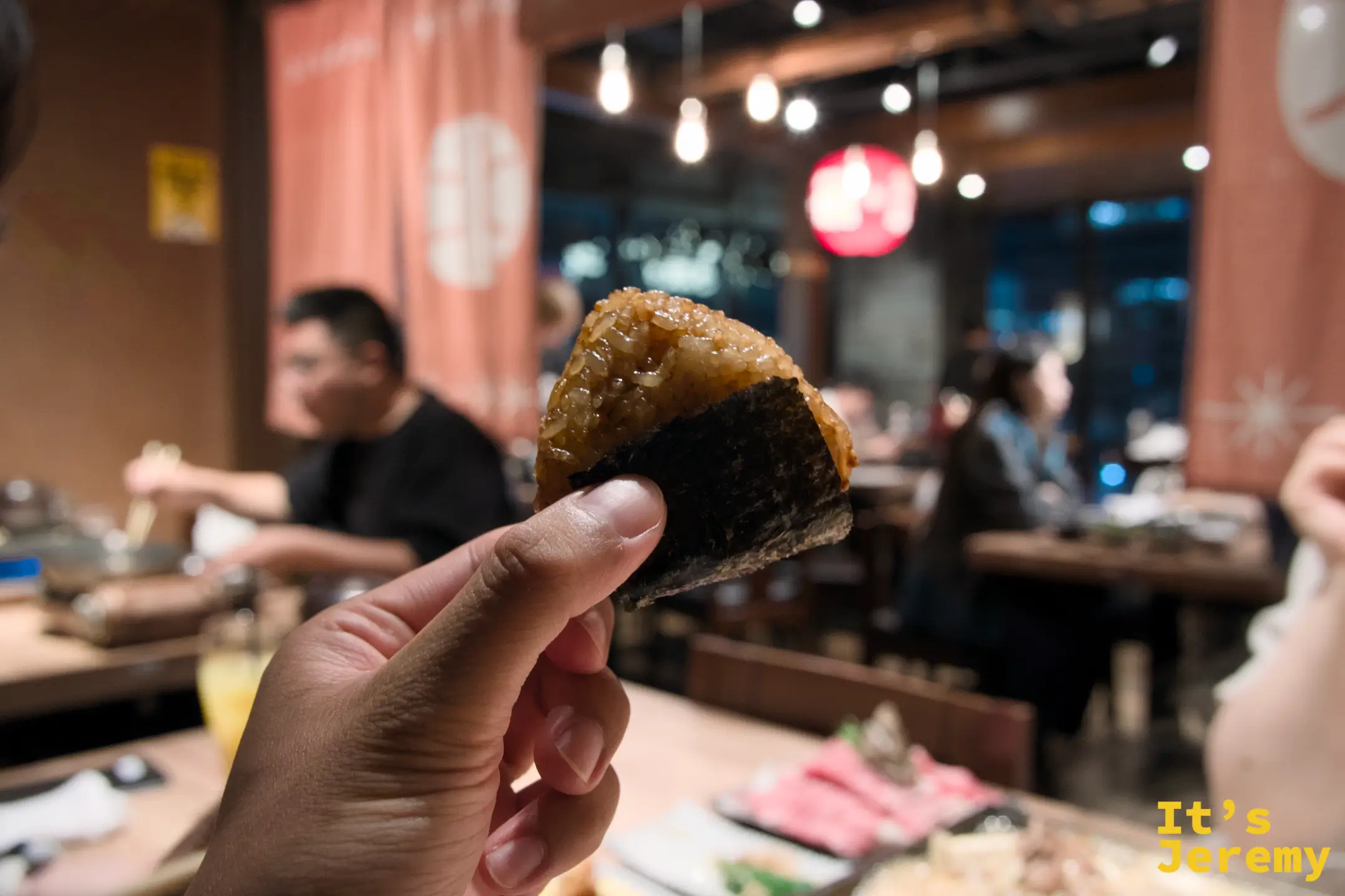 手持烤飯糰，展示焦香表面與餐廳氛圍