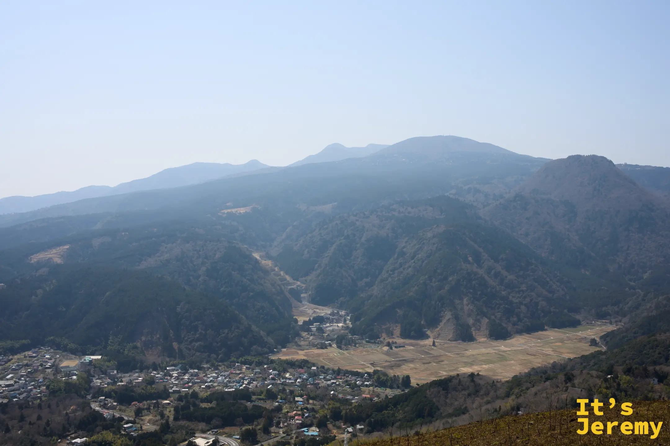 從山頂稜線俯瞰伊豆山間聚落，層疊的山脈向內陸延伸，山谷中有農田與村落