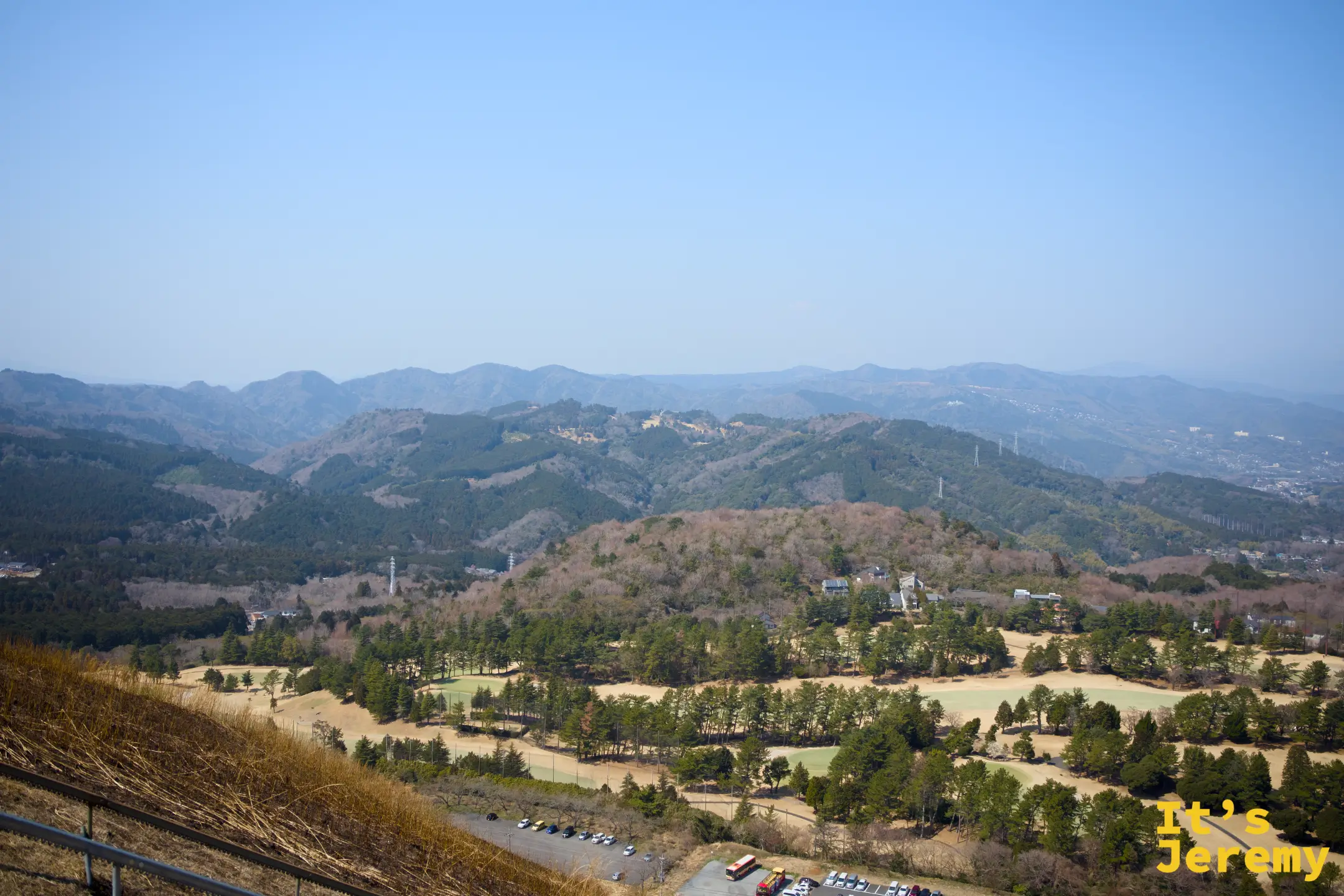 從山頂俯瞰伊東市與周邊山脈，高爾夫球場草地在中景，山脈向遠處連綿