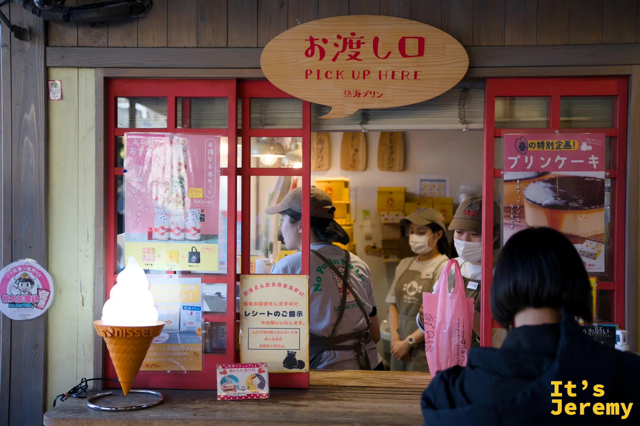 熱海プリン取餐口外觀，木牌寫著お渡し口 PICK UP HERE，旁邊有軟冰淇淋展示模型